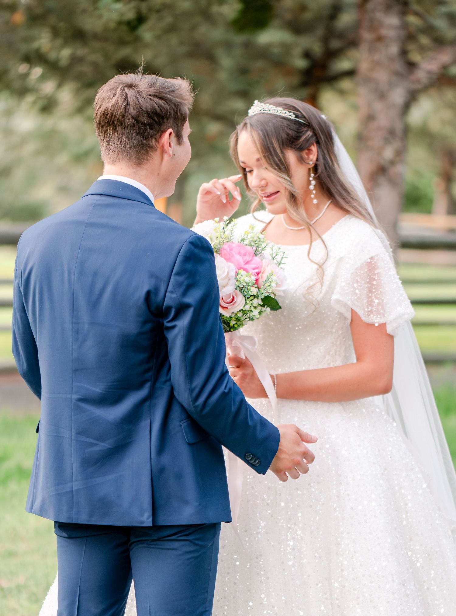 Wedding couple embraces in a garden setting wearing blue suit and white lace dress.