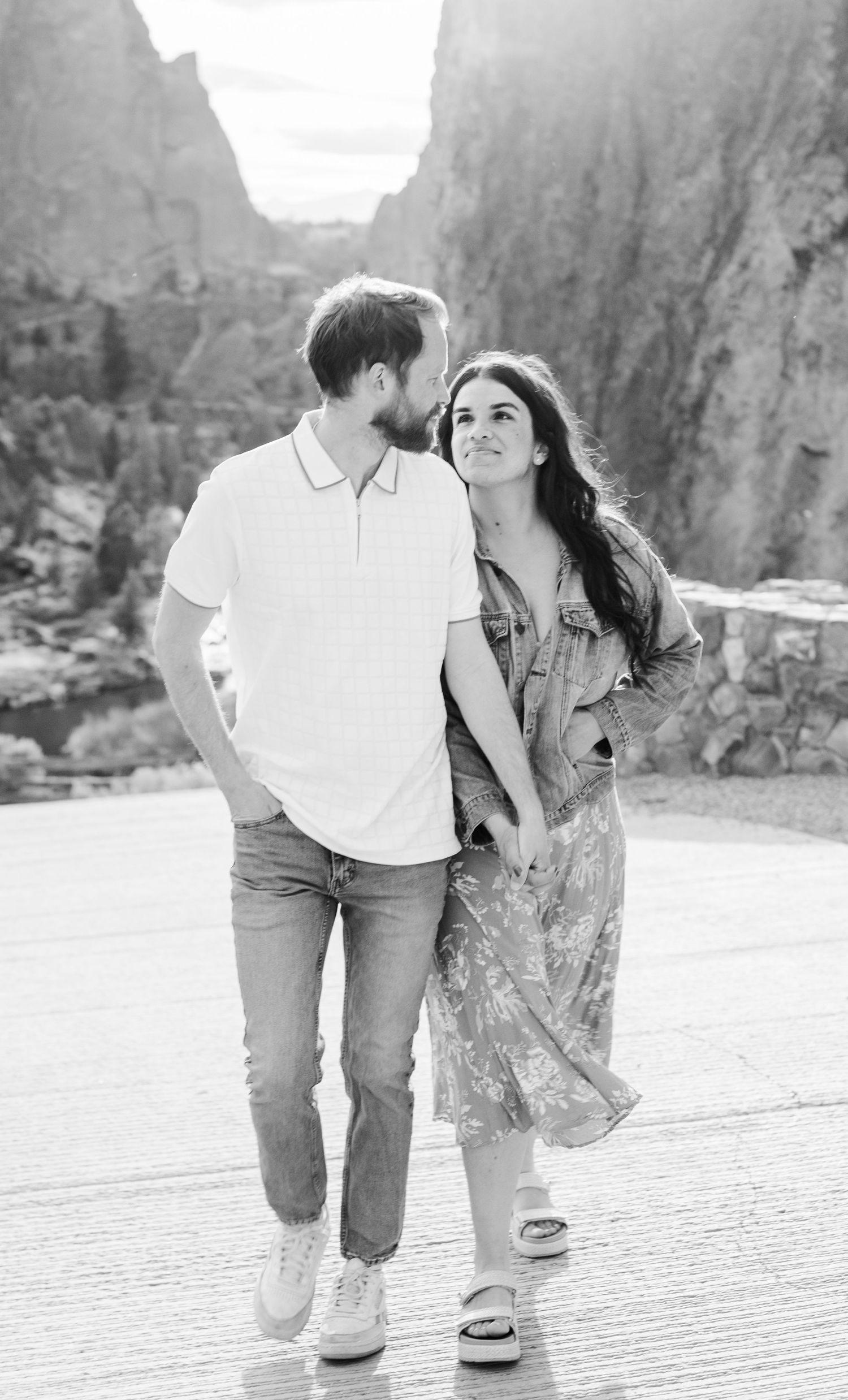 Black and white photo of a couple walking hand in hand with rocky canyon cliffs behind them.