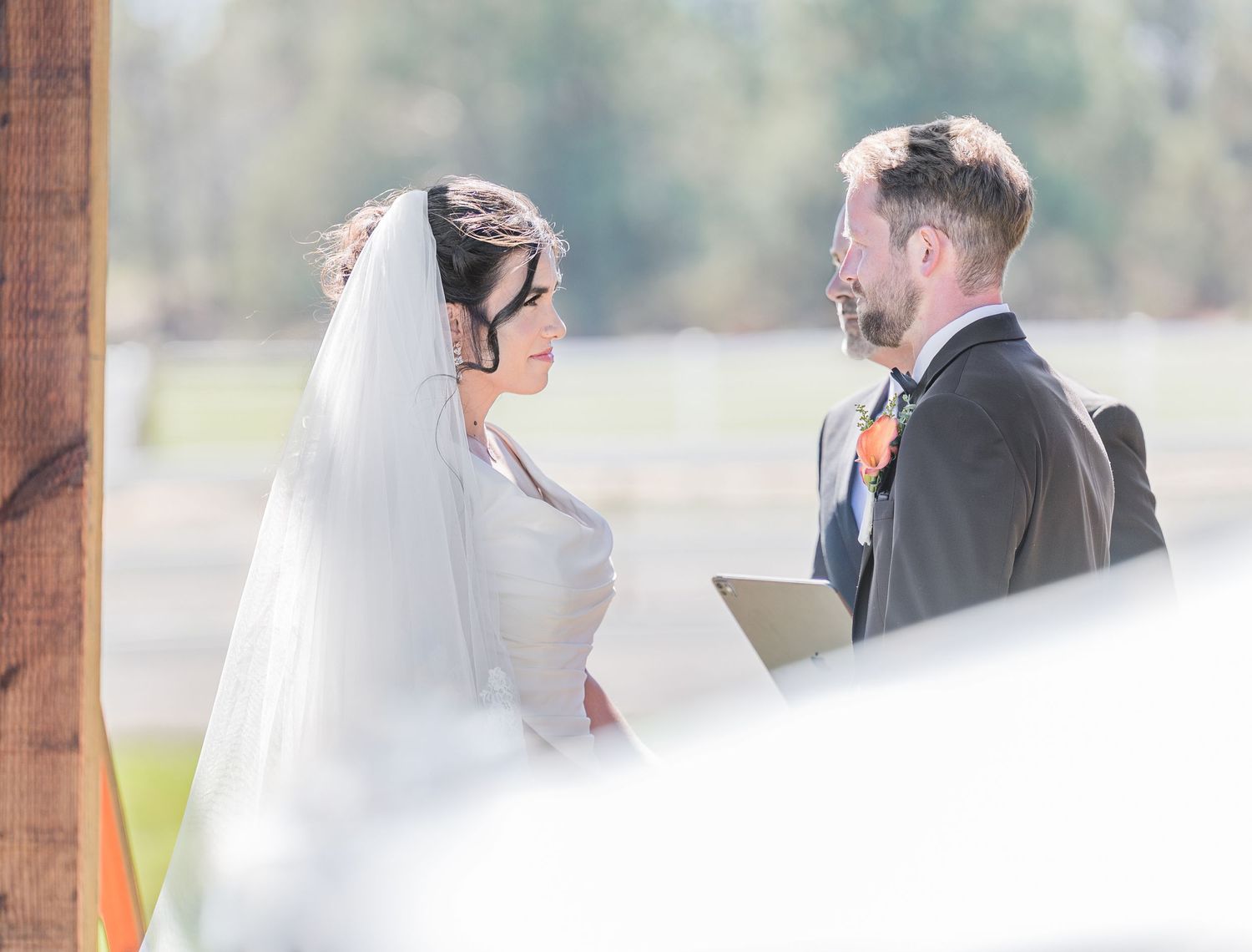 Bride and groom exchanging vows outdoors at a wedding ceremony, bride wearing a white veil.