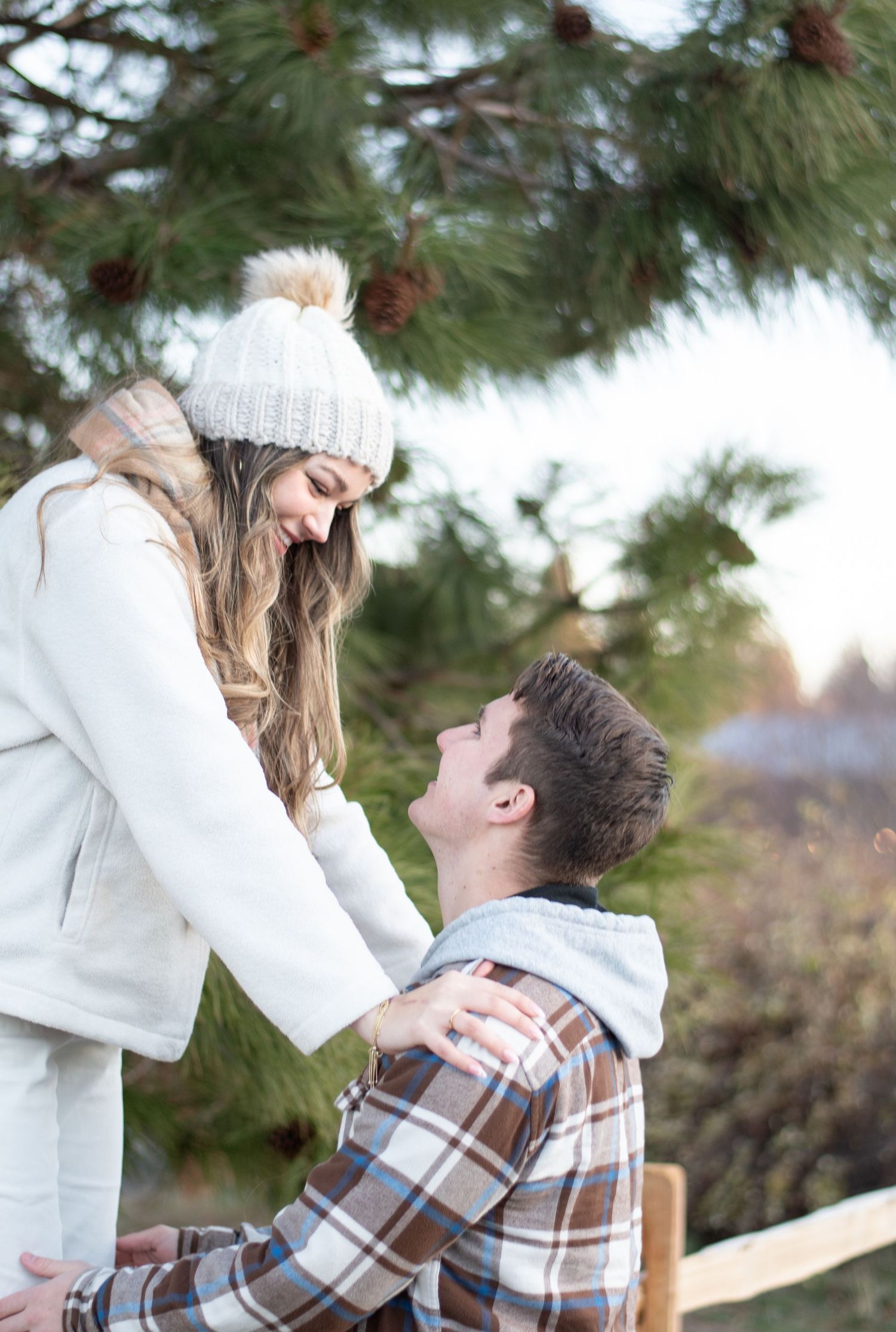 Romantic outdoor photo shoot under pine trees in winter clothing.