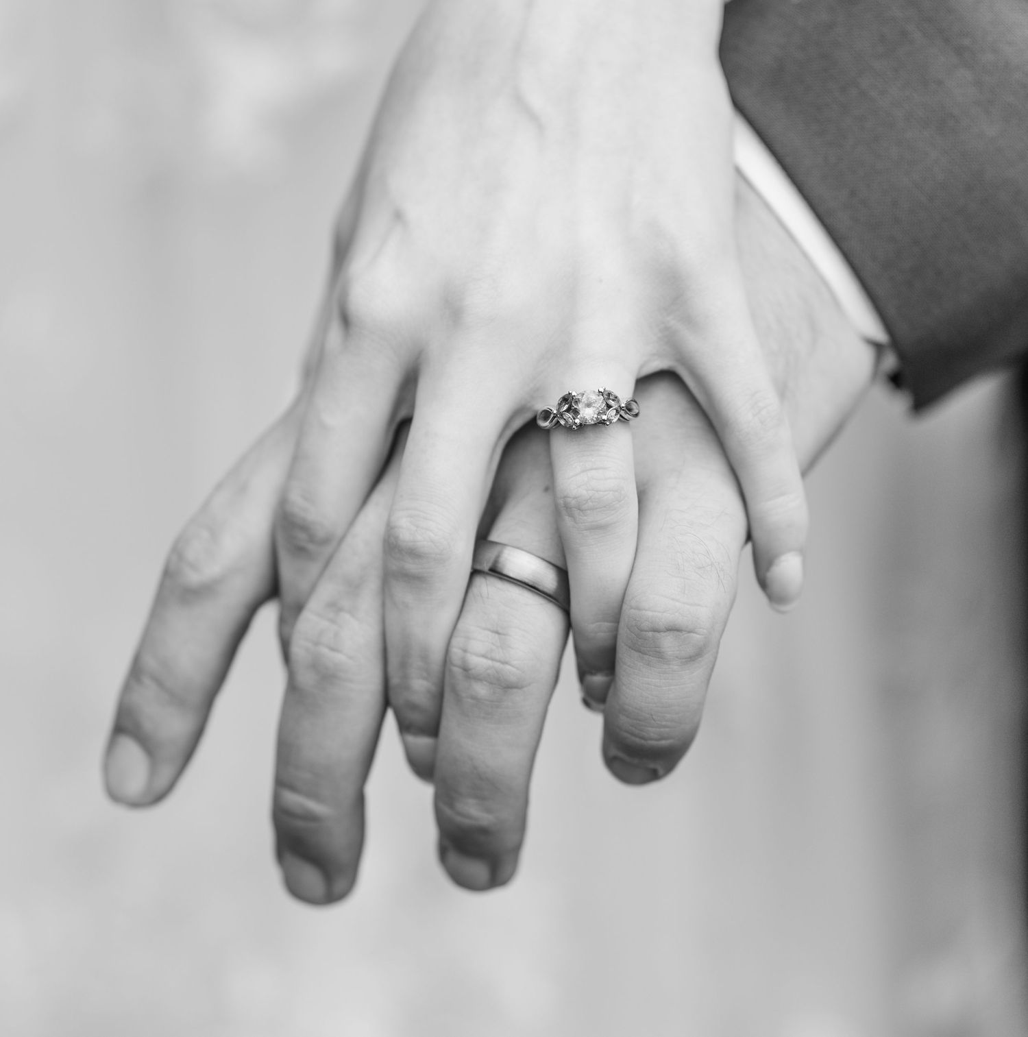 Black and white close-up of a bride's hand with an engagement ring resting on a groom's hand with a wedding band.