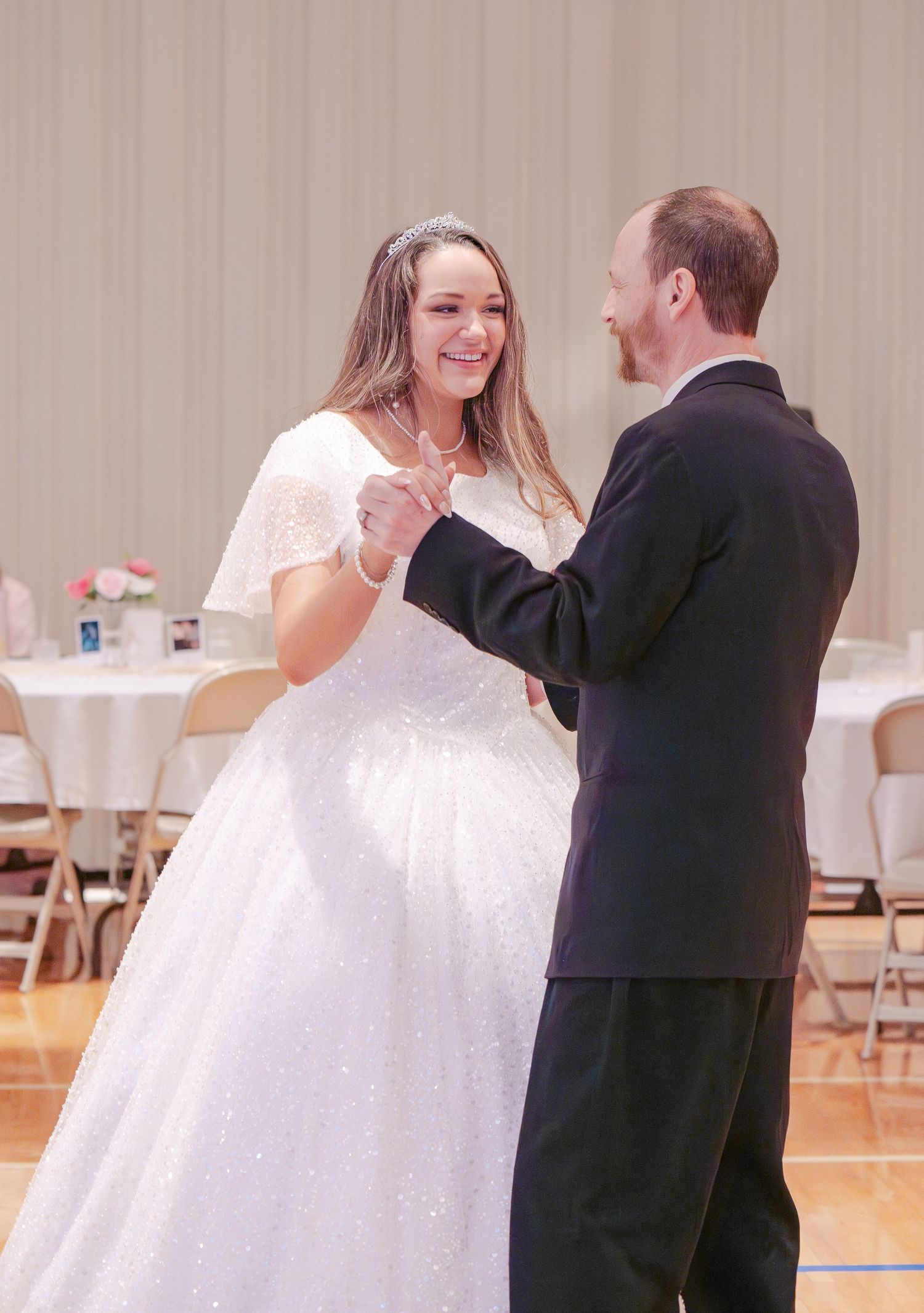 Couple shares a romantic dance moment at their wedding reception in a bright gymnasium setting.