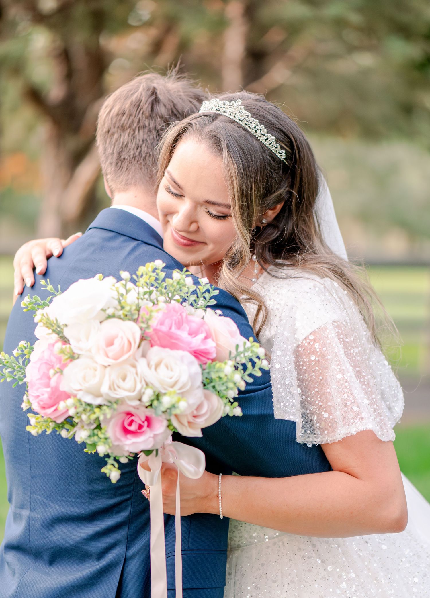 Emotional wedding embrace captured with pink and white florals in outdoor garden setting.