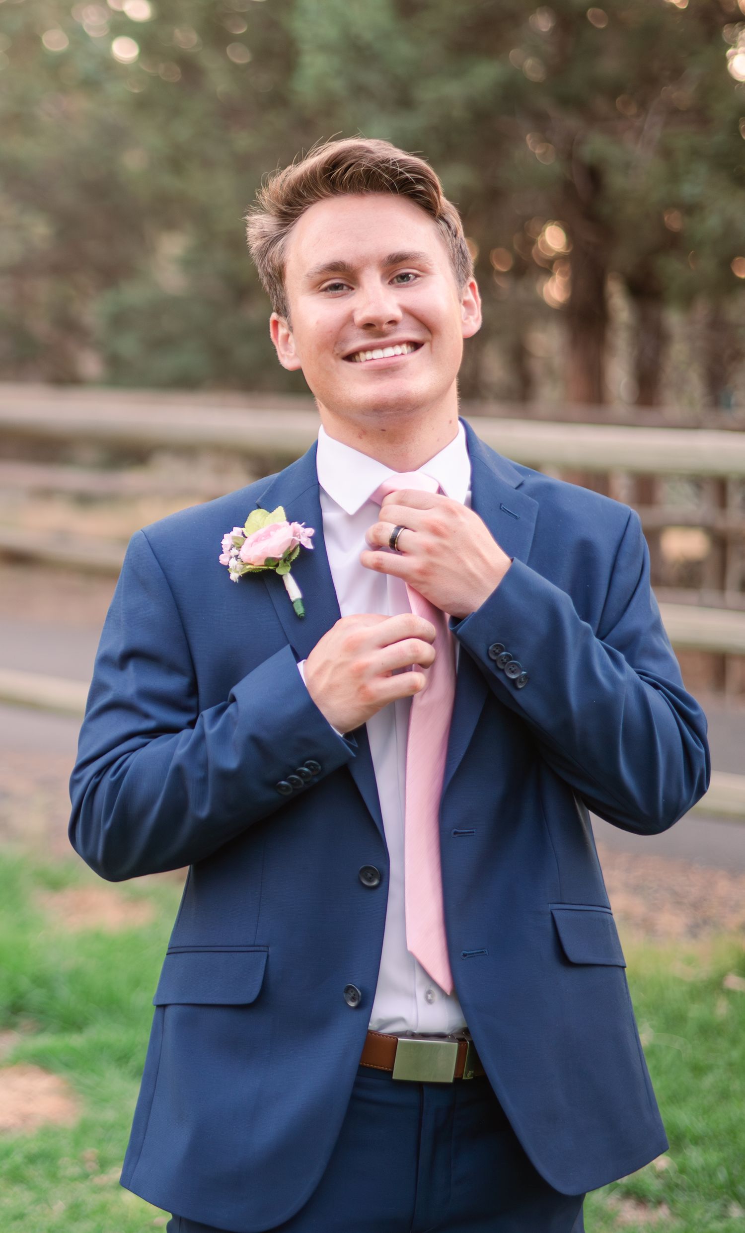Groom in navy suit with pink tie shows joyful emotion during outdoor wedding portraits.