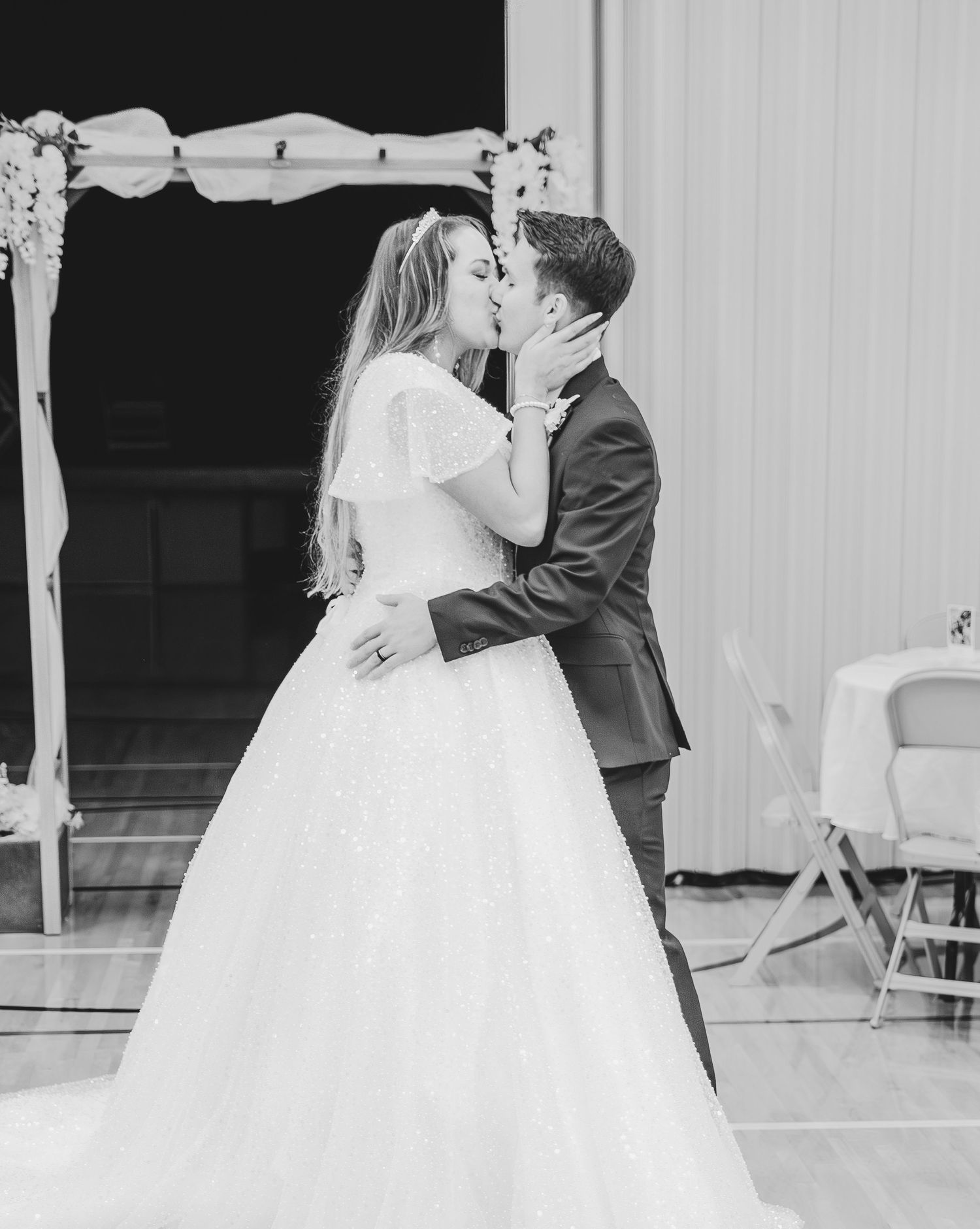 Black and white wedding photo showing a couple dancing together under decorative white arches.