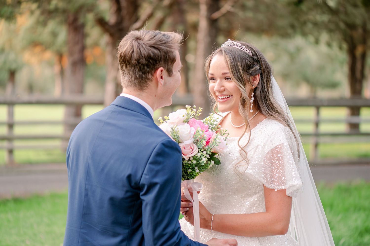 Romantic wedding couple shares intimate moments in an outdoor garden setting with pink floral bouquet.