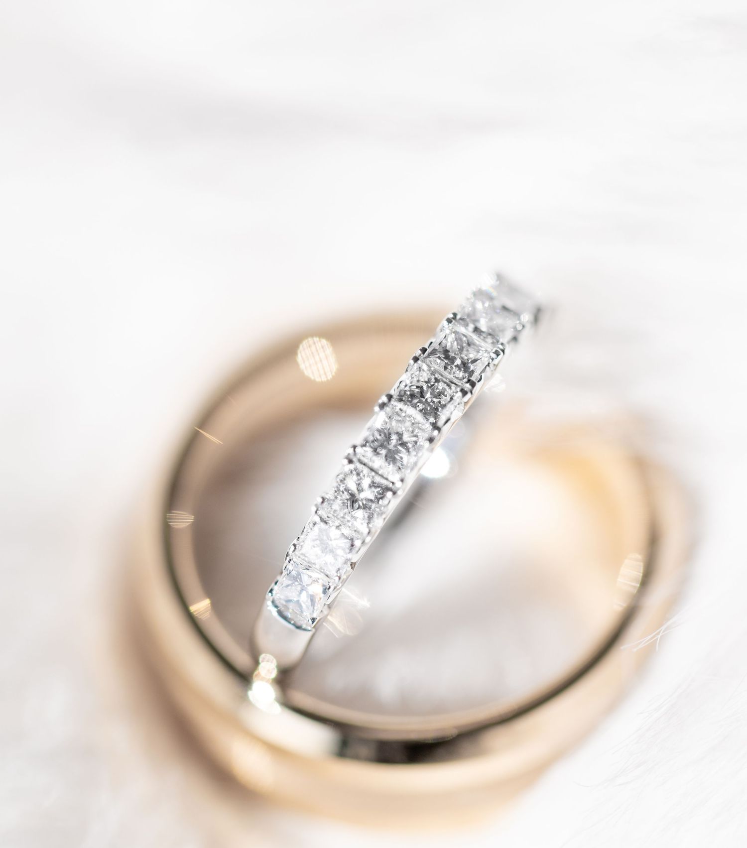 Diamond eternity band ring resting on gold wedding bands, close-up macro jewelry photography on white fabric.
