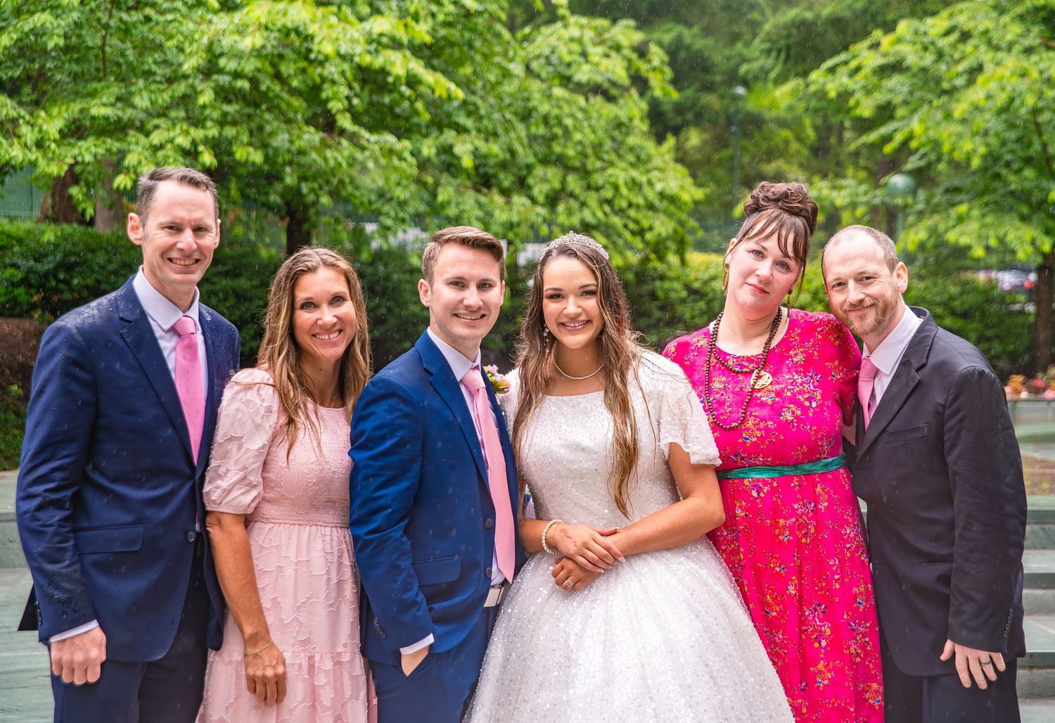 Small wedding group poses outdoors wearing coordinated navy and pink attire.