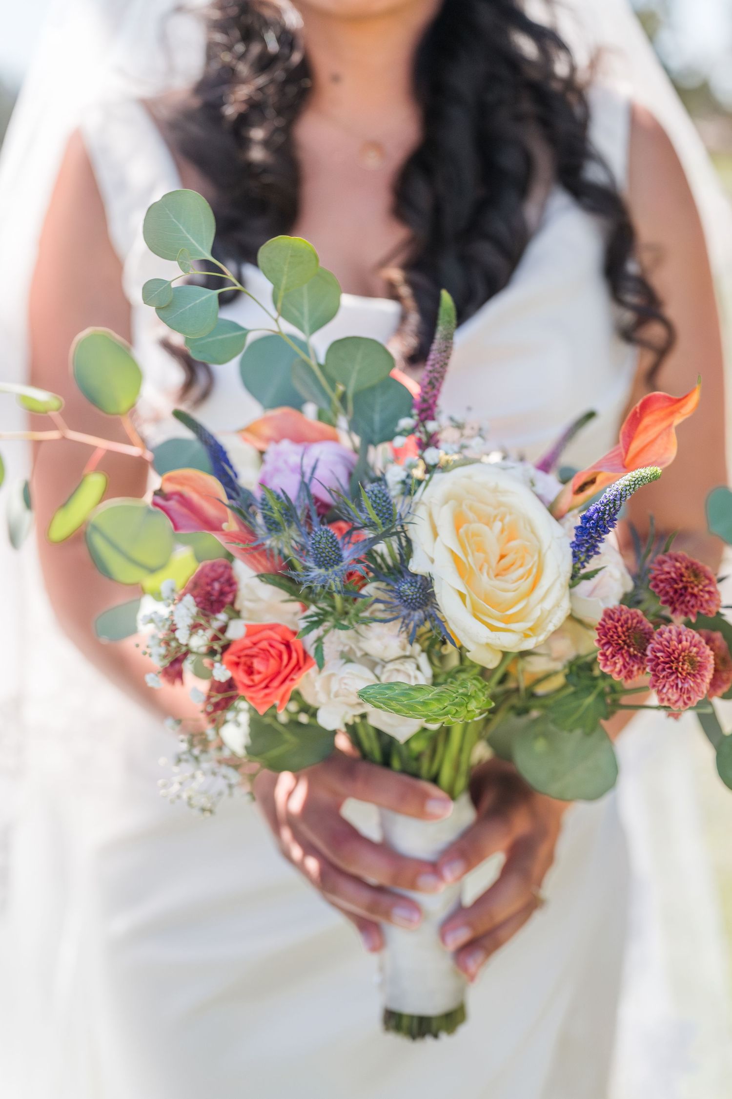 Bride in white dress holding a colorful wedding bouquet with roses, eucalyptus, and wildflowers.