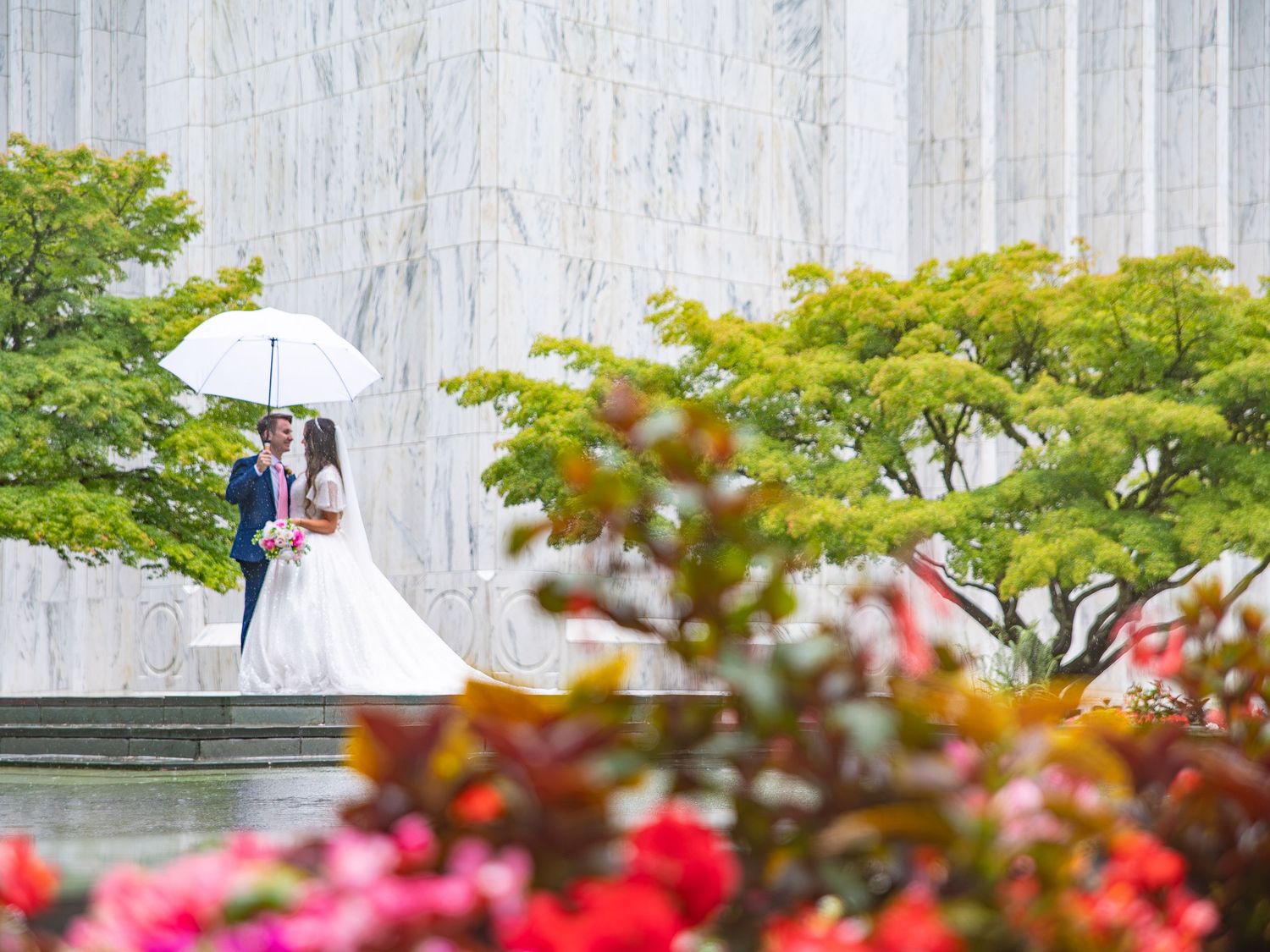 White temple building framed by colorful flowers and green trees.