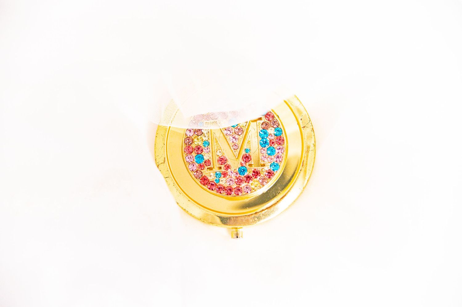 Gold compact mirror with colorful sprinkle details photographed on white background.