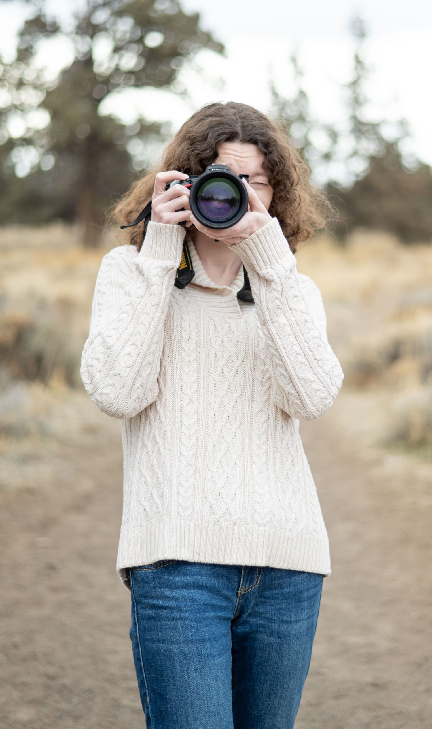Person in cream sweater holding camera in natural outdoor setting.