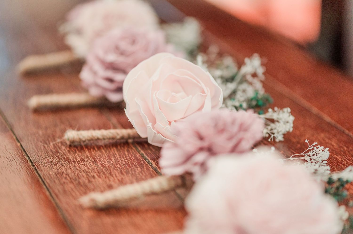 Pink rose and baby's breath boutonnieres with twine wrap displayed on wooden surface for wedding.