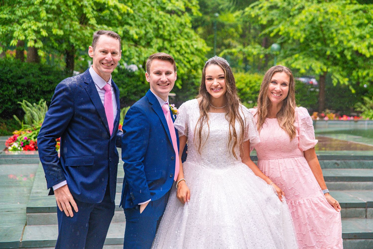 Wedding party members in navy suits and pink dresses pose with bride on stone steps.
