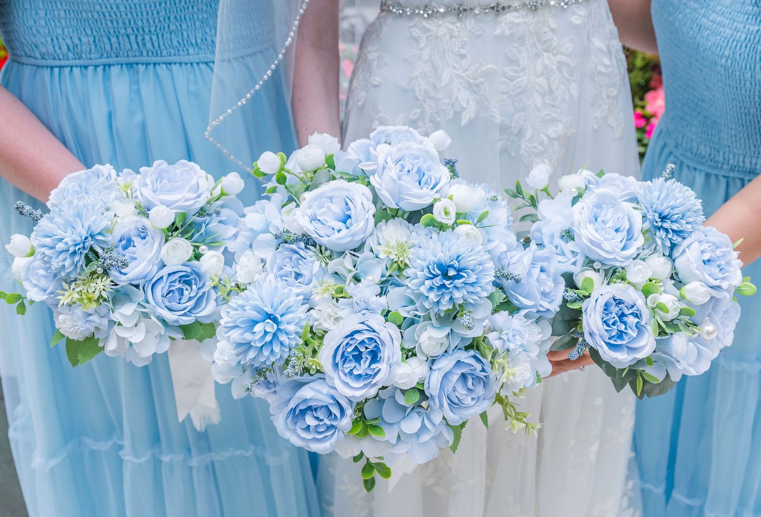 Bridesmaids holding elegant light blue floral bouquets with roses and hydrangeas at a wedding ceremony.