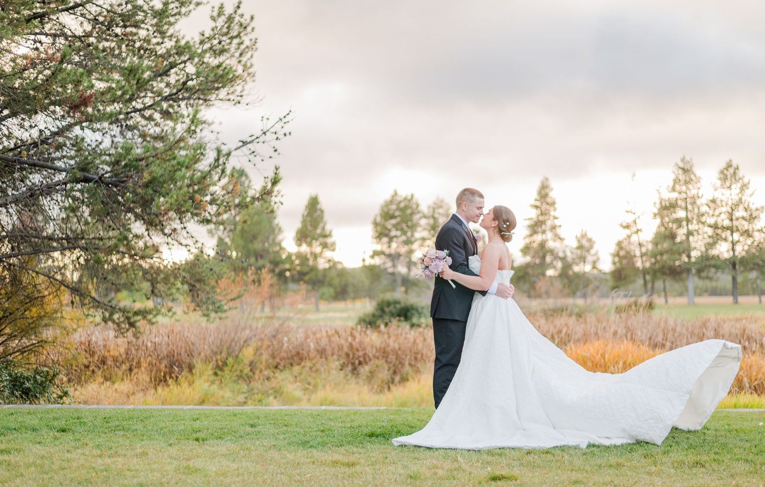 Golden hour wedding portraits in rustic field setting with dramatic sunset sky.