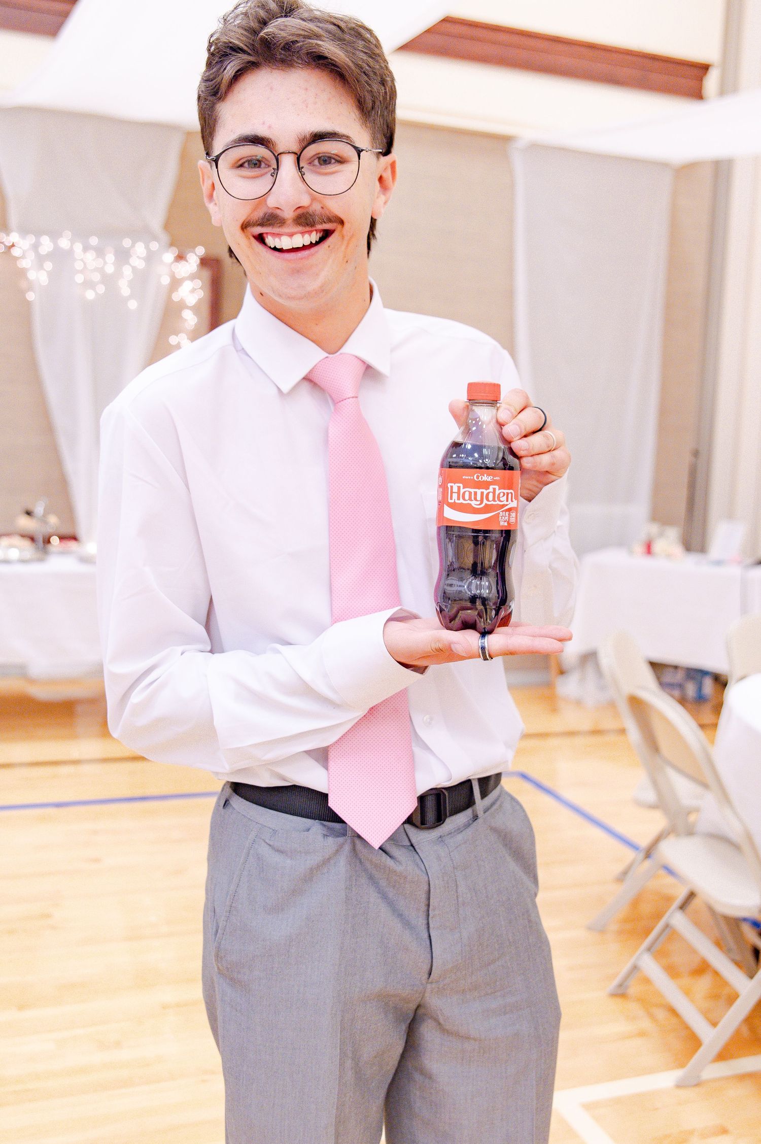 Wedding guest in grey pants and pink tie holds up a drink while smiling at reception.