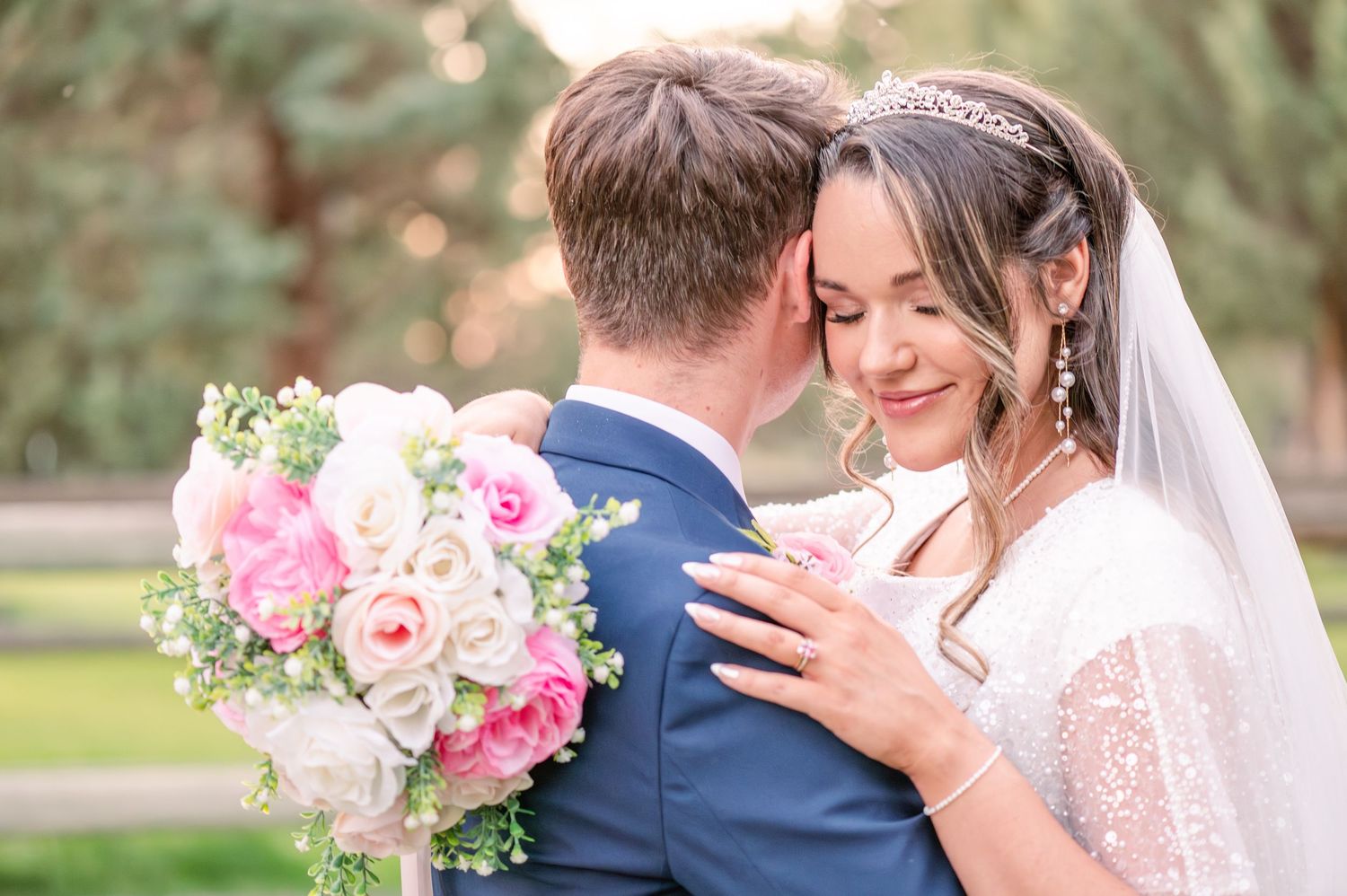 Tender wedding moment captured in natural outdoor setting with soft lighting and floral details.