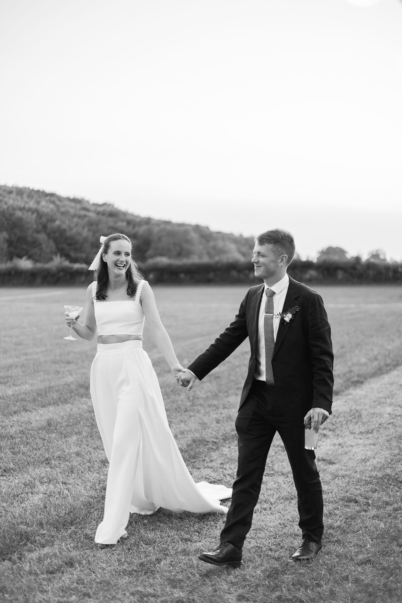 A couple in wedding attire dances joyfully together in a grassy field on their special day.