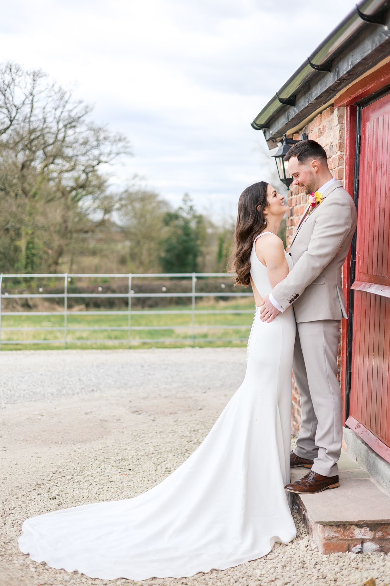 Wedding couple shares an intimate moment in front of a rustic red barn door as her white train dress flows behind.