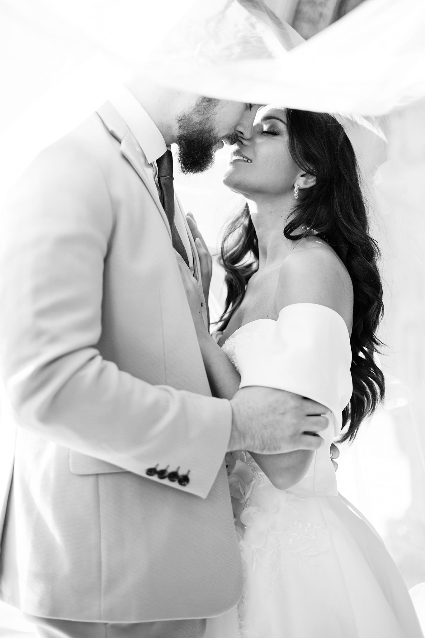 A romantic black and white wedding photo capturing a tender moment between a couple in elegant white attire.
