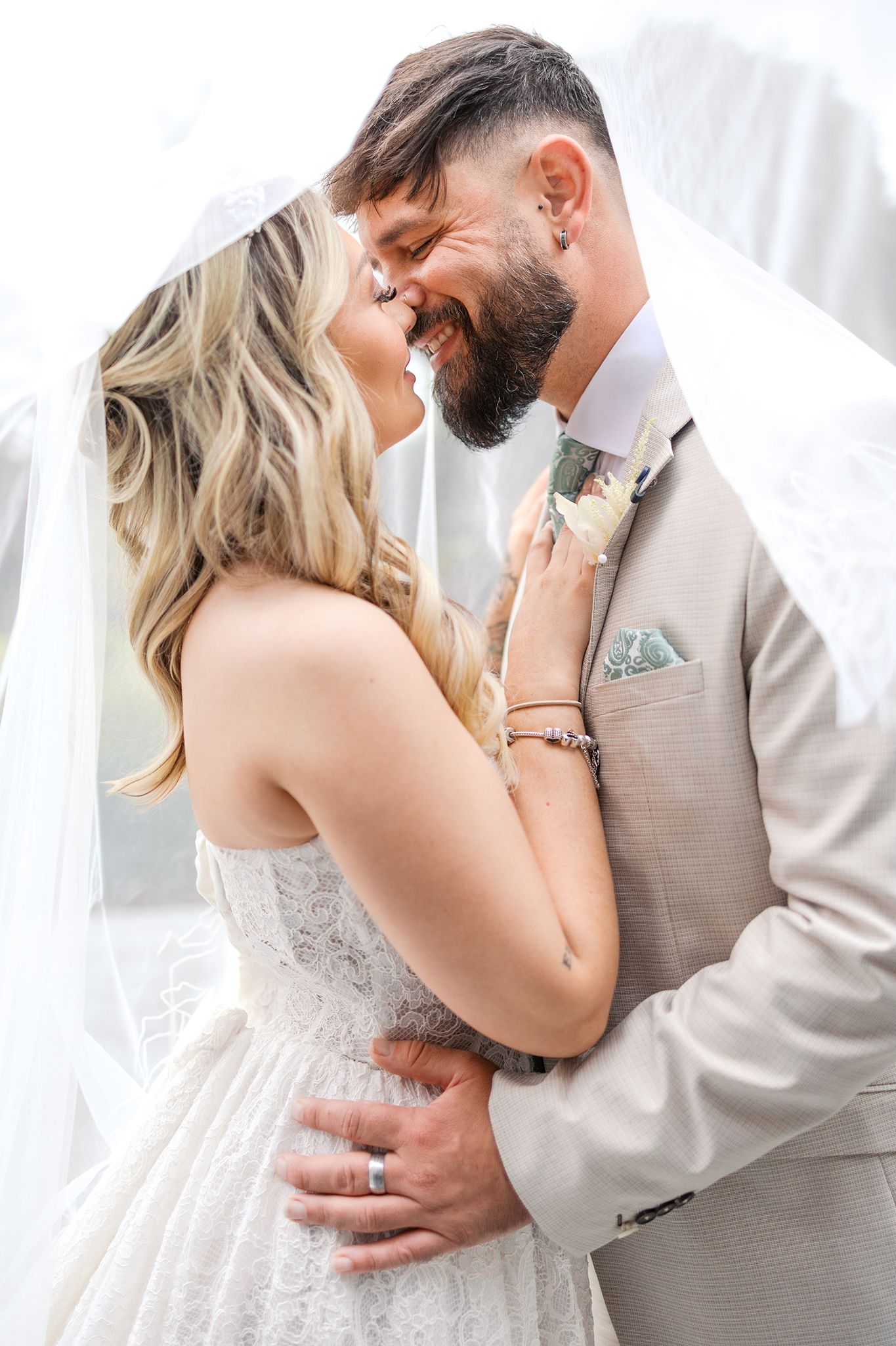 A romantic wedding couple shares an intimate moment against white curtains and soft lighting.