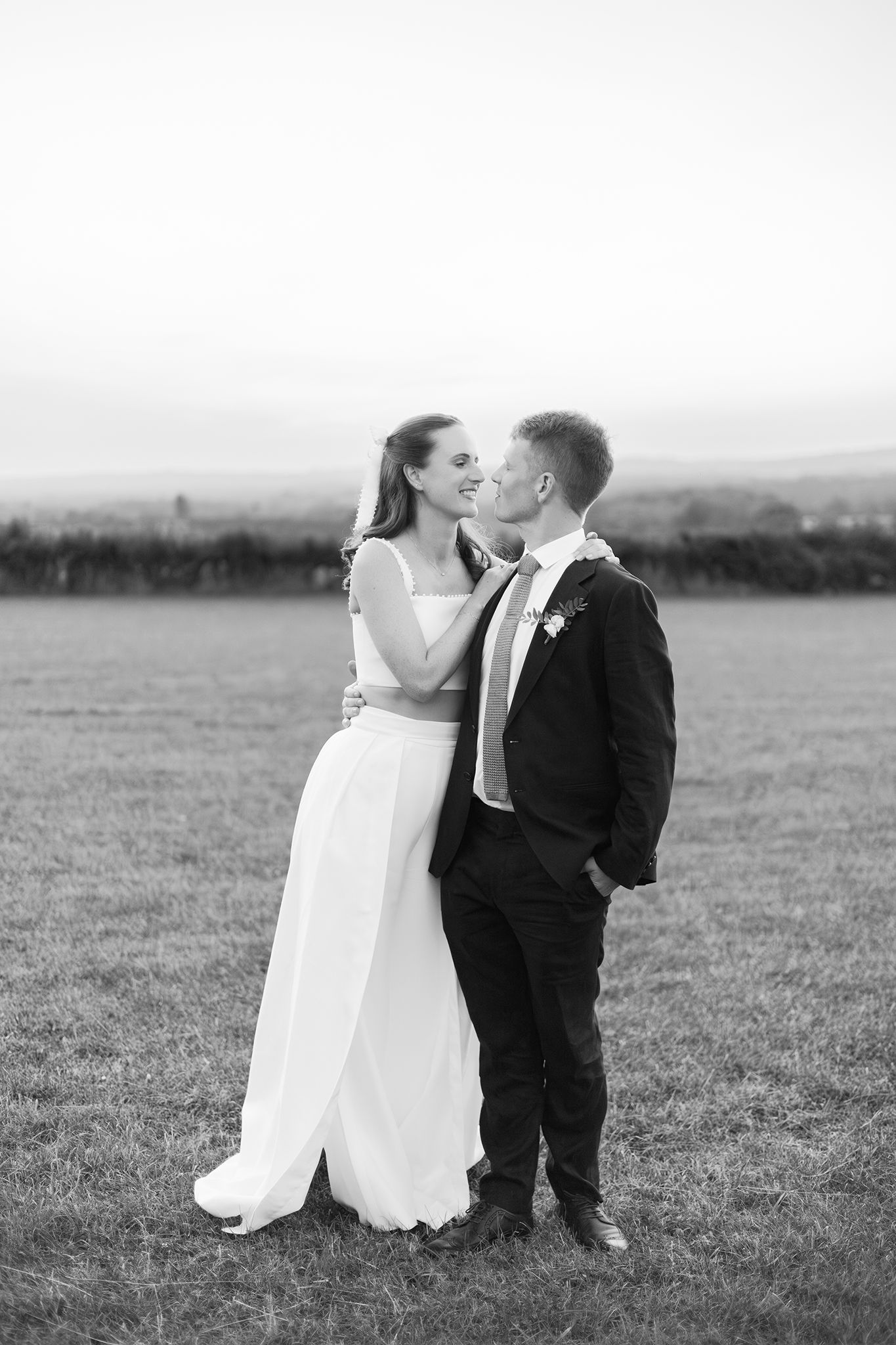 A romantic black and white wedding photo series showing a couple sharing tender kisses in an open field.
