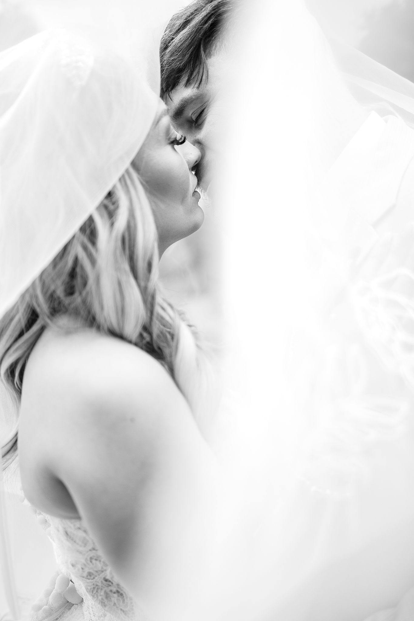 Monochromatic side profile wedding portrait showing a bride in a lace gown with a flowing veil.