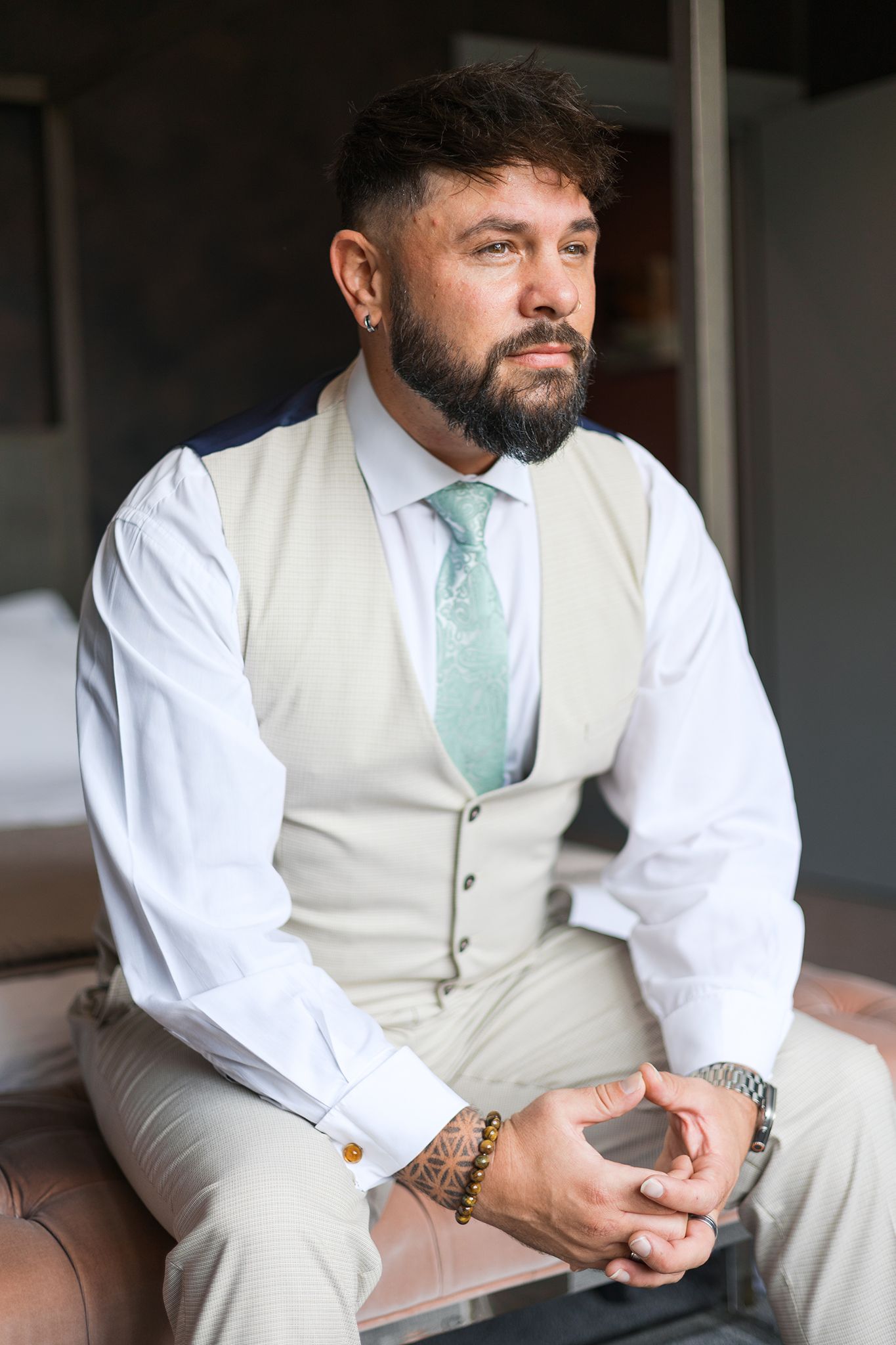Close-up views of someone wearing a beige vest and white shirt with mint green tie sitting in profile against a dark background.