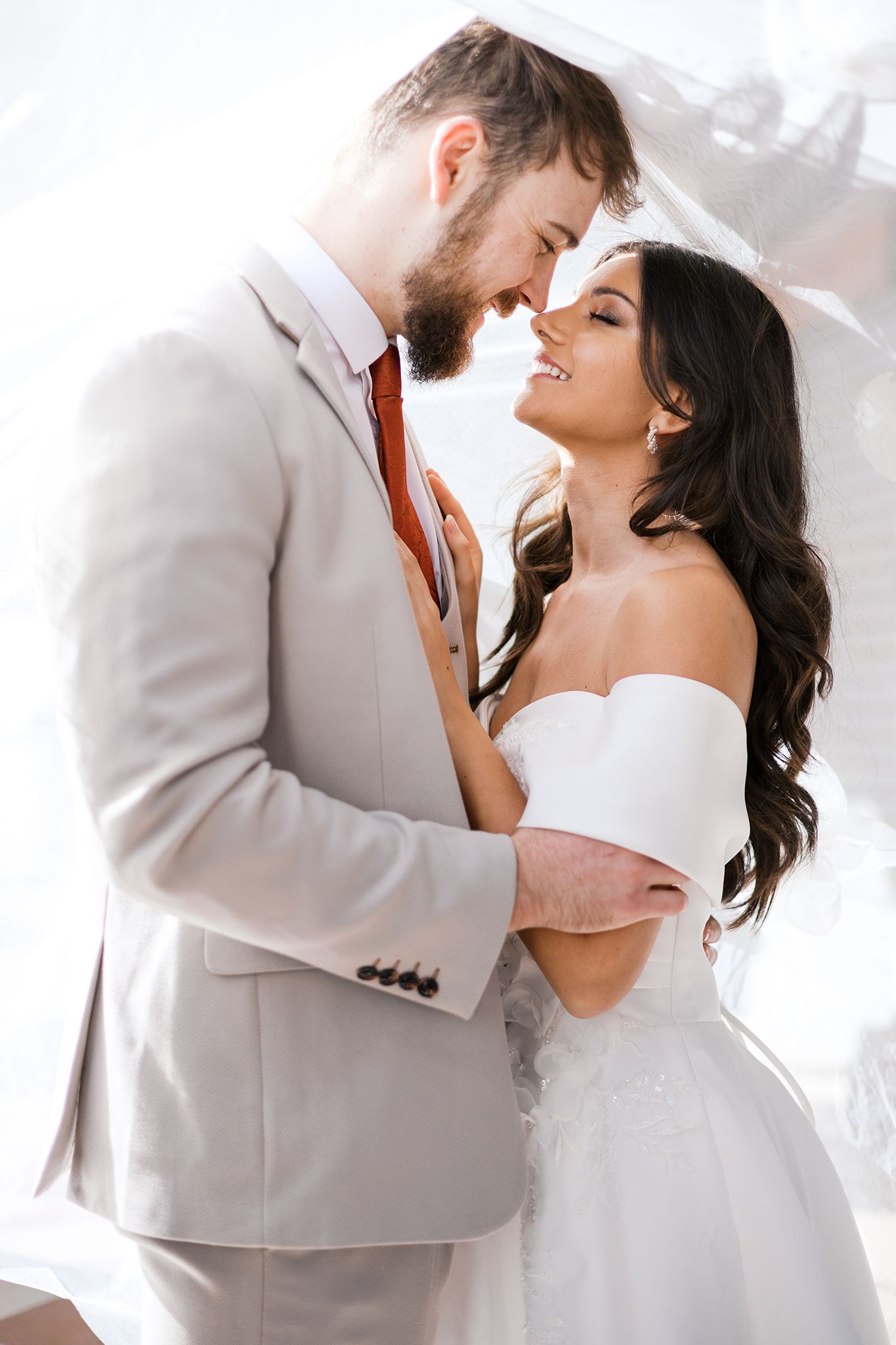 A romantic wedding moment captured between a couple in light-colored attire sharing an intimate pose against a bright background.