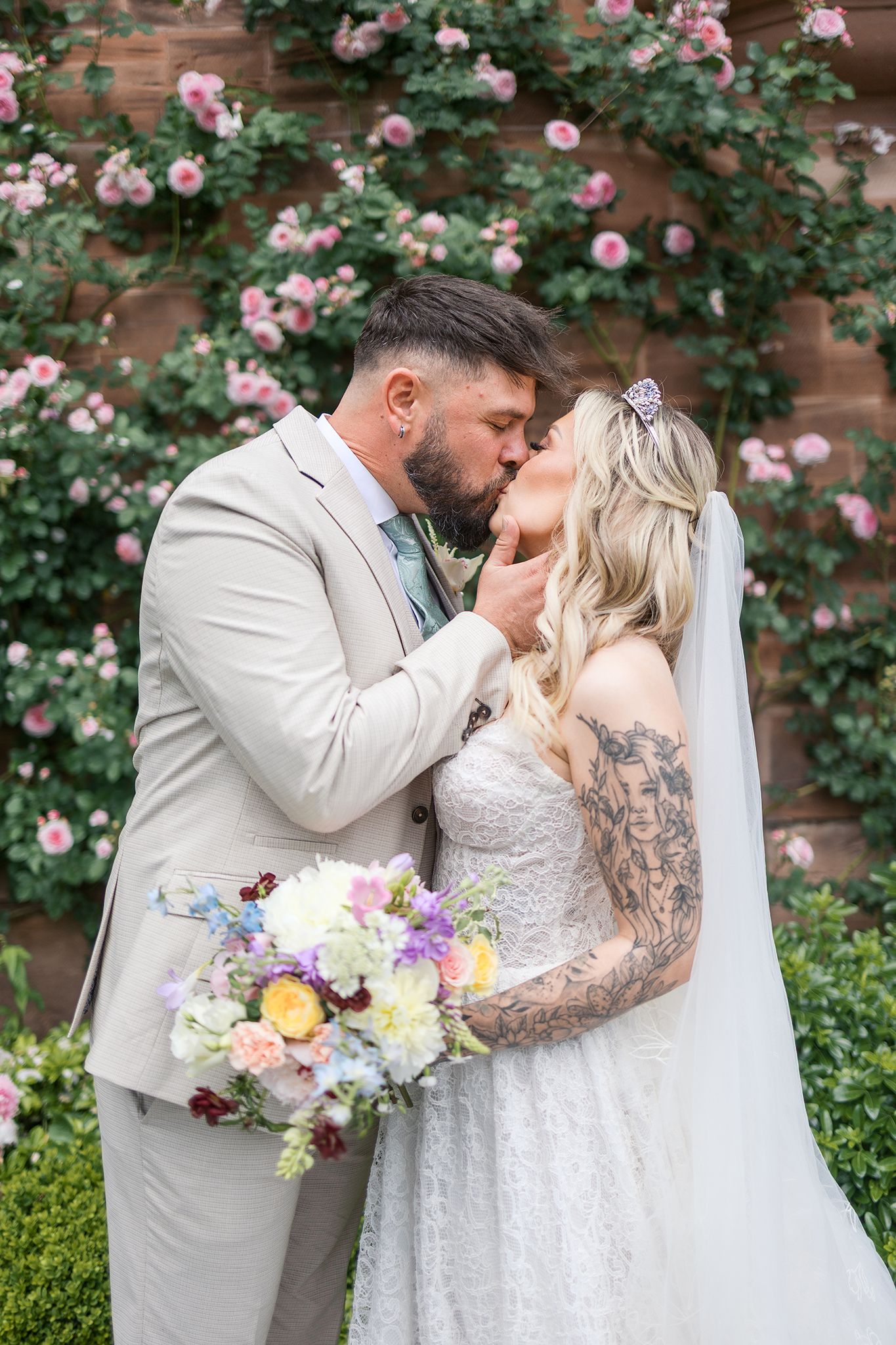 A romantic wedding moment captured among pink roses and lush greenery during a spring garden ceremony.