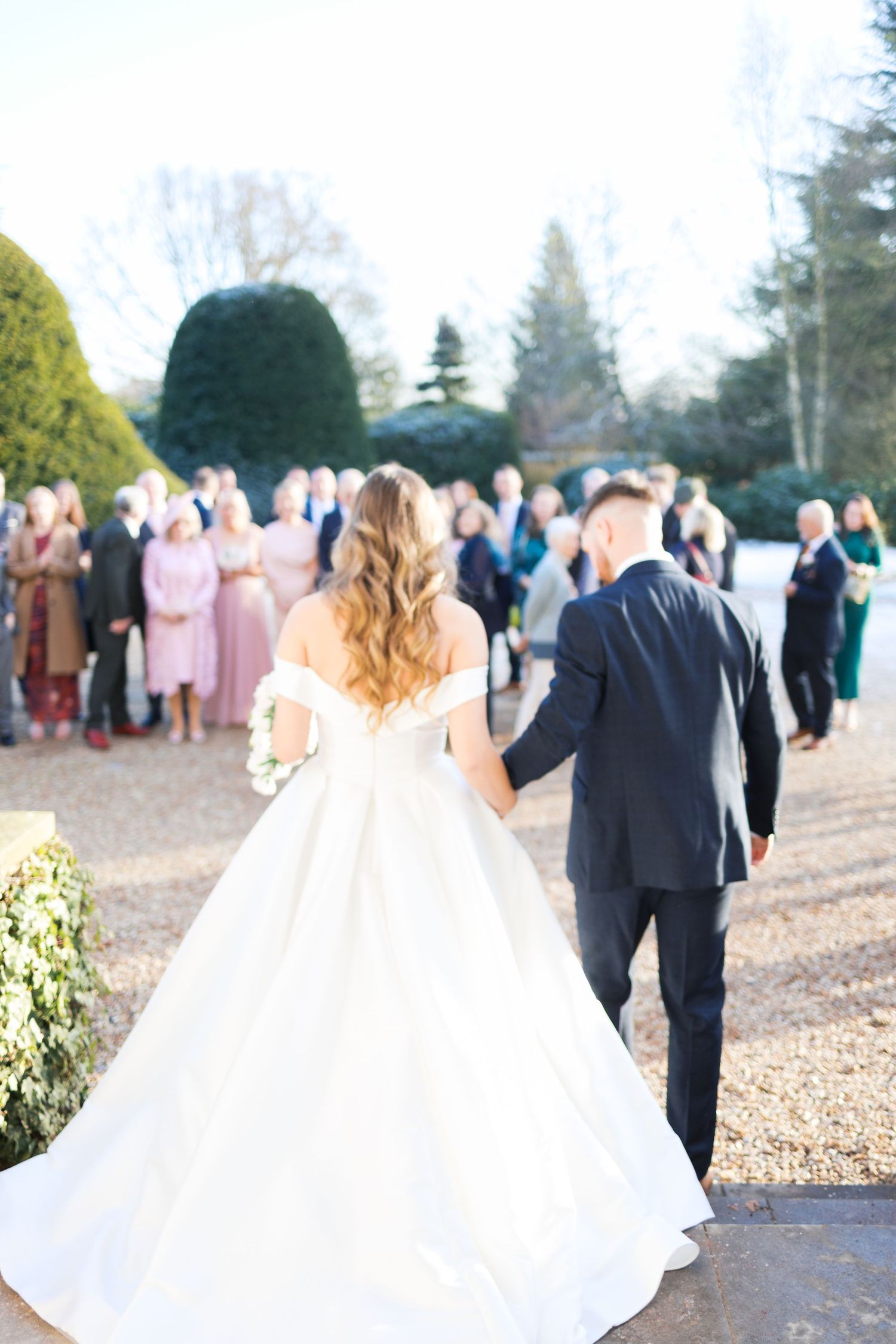 A bride and groom walk away from their wedding ceremony as guests look on in the background.