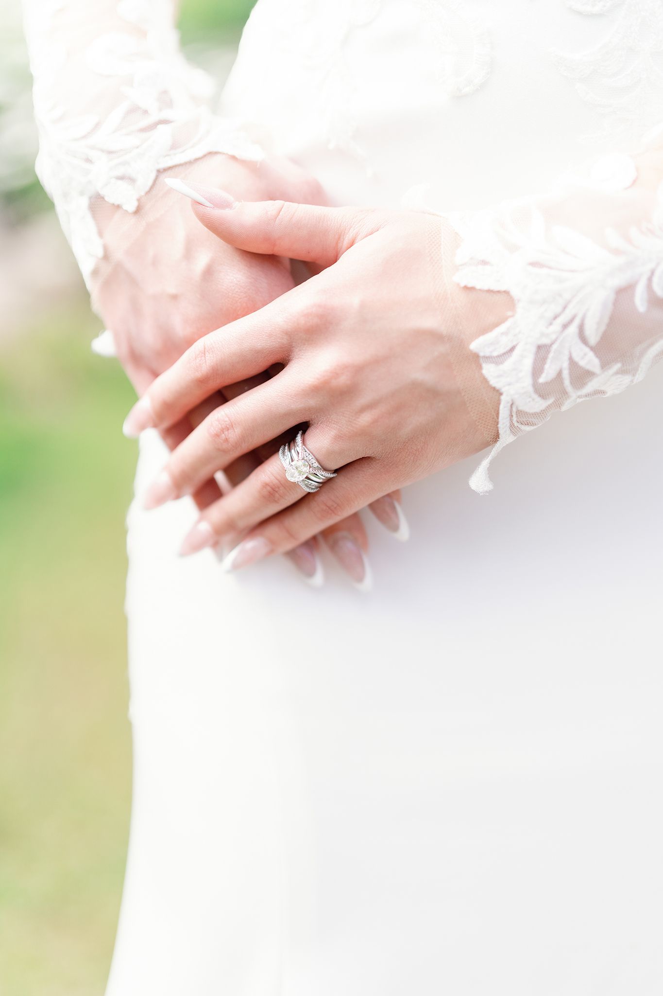 Bride in lace wedding dress with clasped hands showing a sparkling diamond engagement ring.