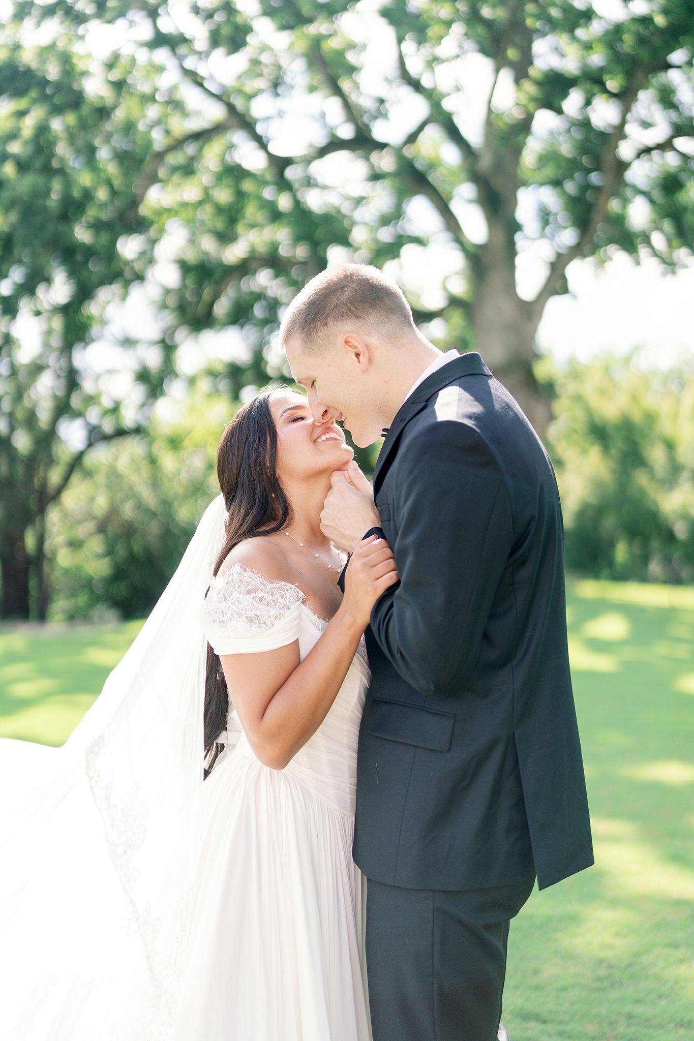 A bride and groom share a romantic moment outdoors, surrounded by lush green trees on their wedding day.