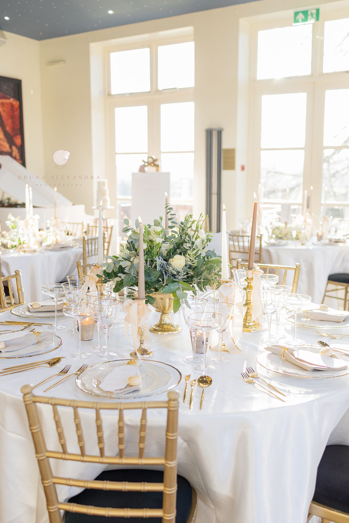 An elegant wedding reception table setting with gold chairs and white linens in a bright venue.
