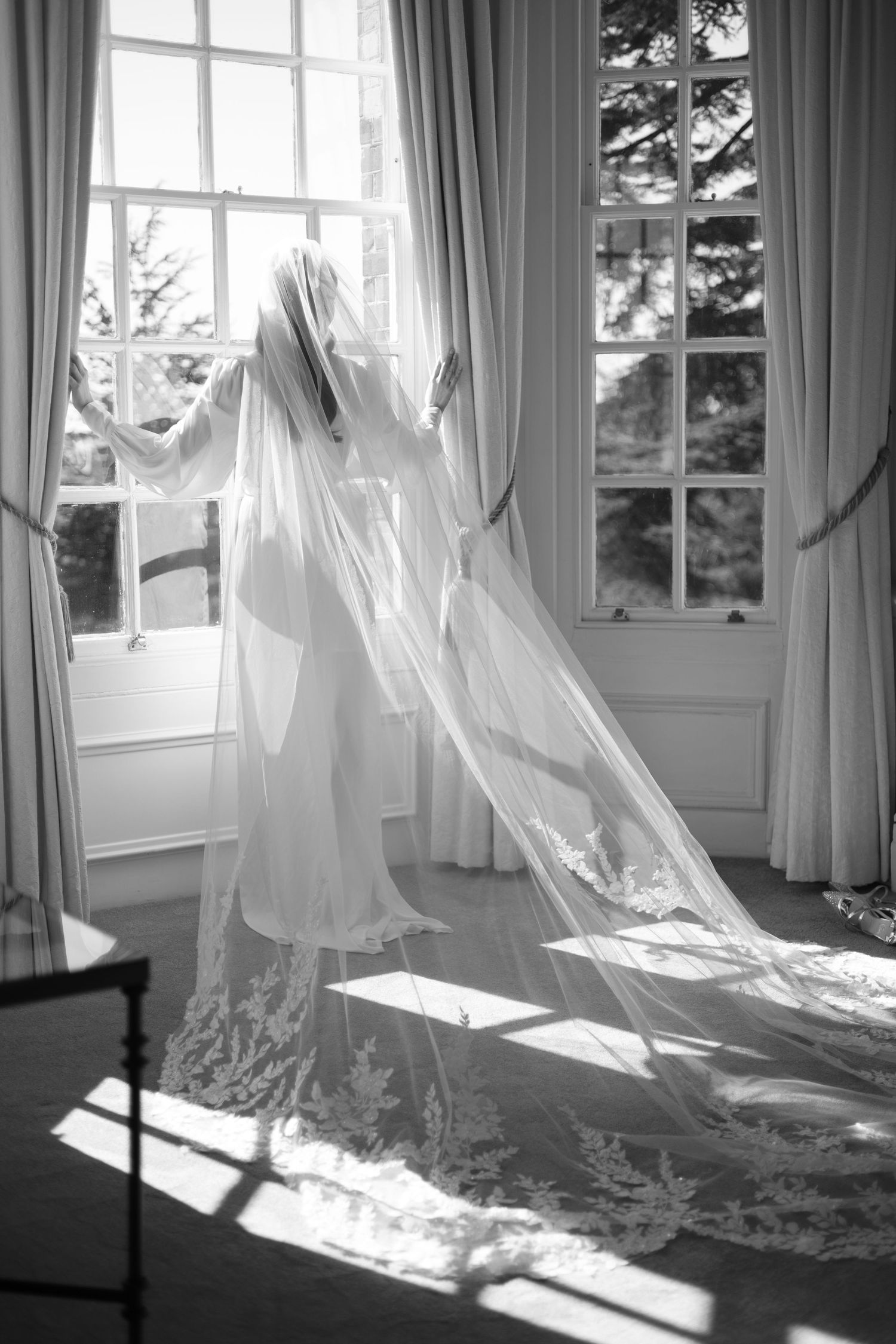 Ethereal white curtains billow in sunlight through multiple windows, creating a dreamy monochrome interior scene.