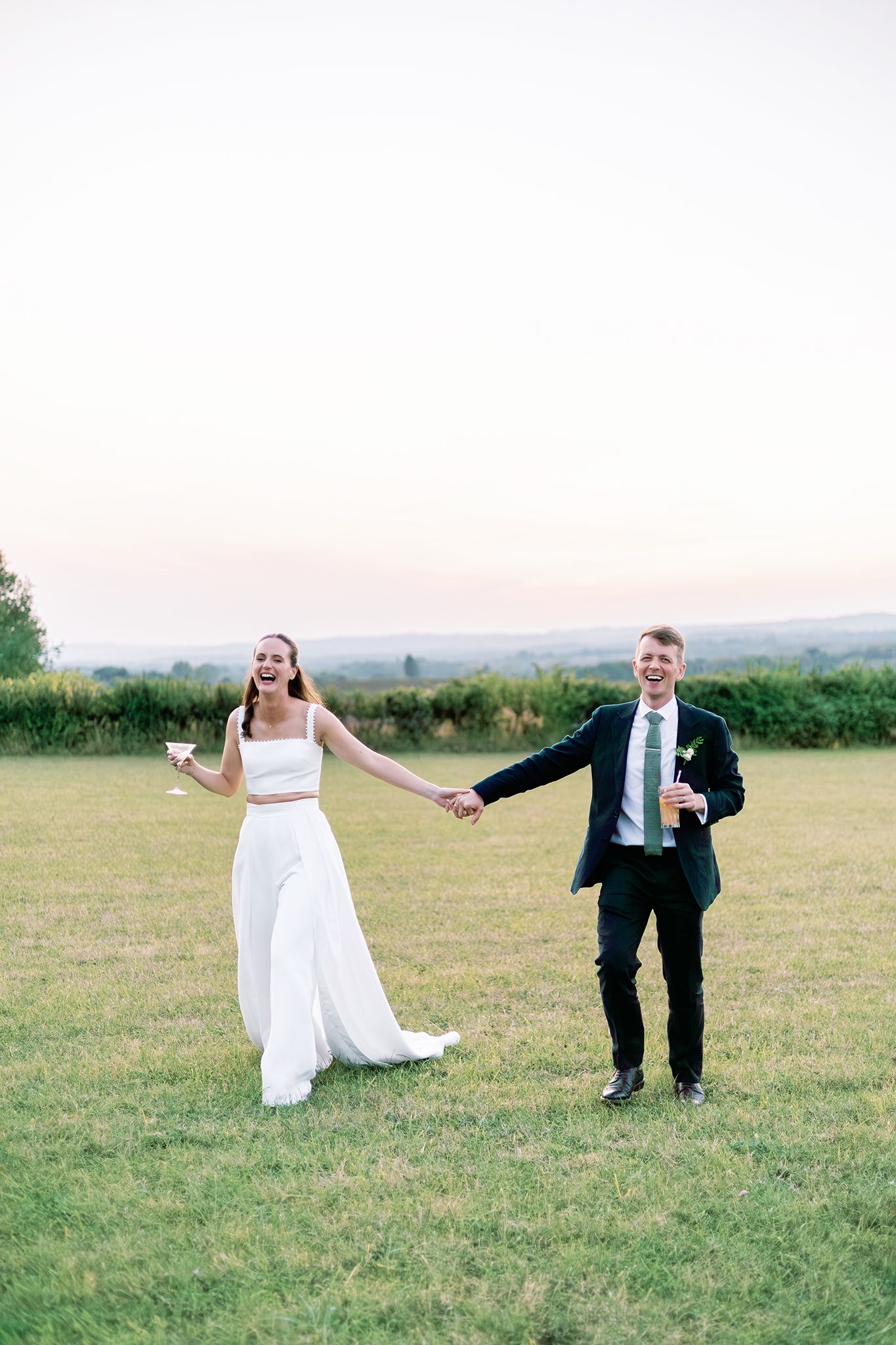 A couple in wedding attire playfully poses in a sequence of photos on a grassy hillside at sunset.