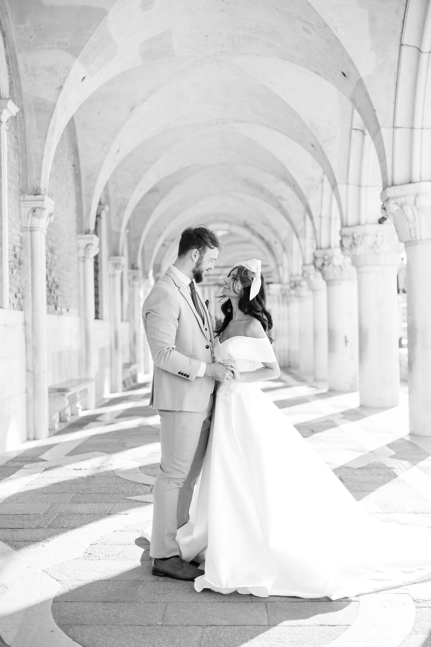 Black and white photo of a bride and groom embracing under elegant arched colonnade in Venice, Italy.