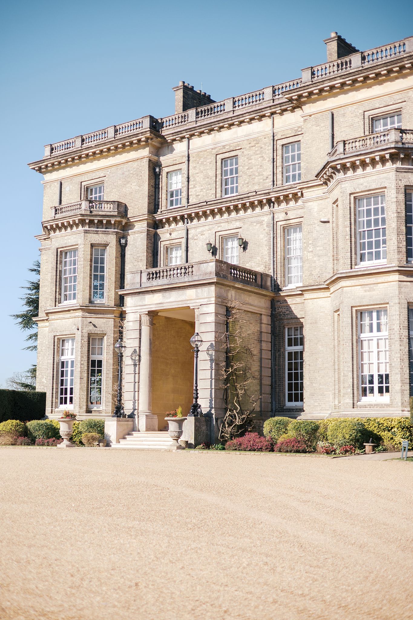 Elegant historic English manor house with grand columns, balustrades and cream-colored stone facade on a sunny day.