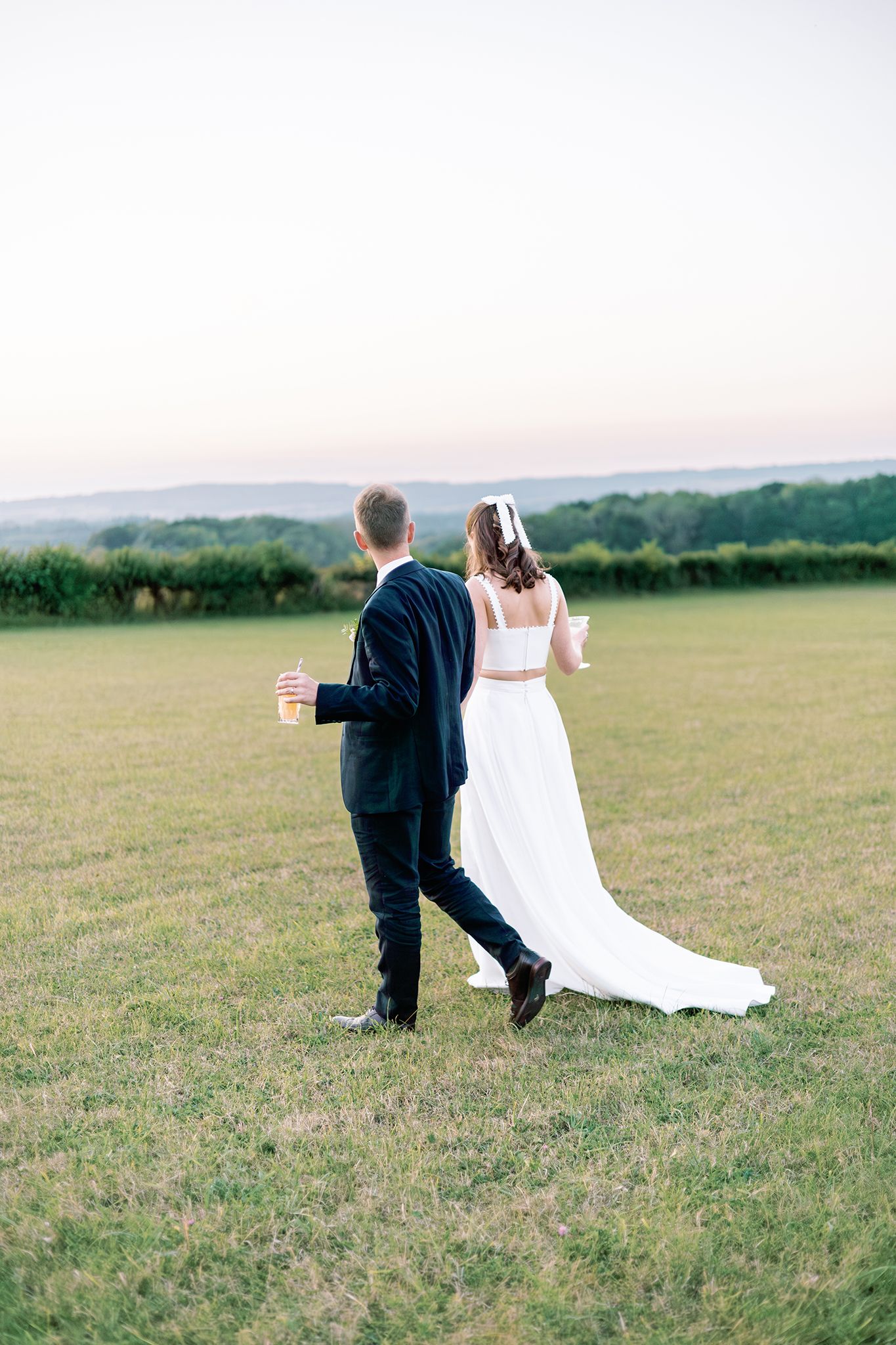 A couple in formal wedding attire playfully rolls down a grassy hillside in a romantic outdoor setting.