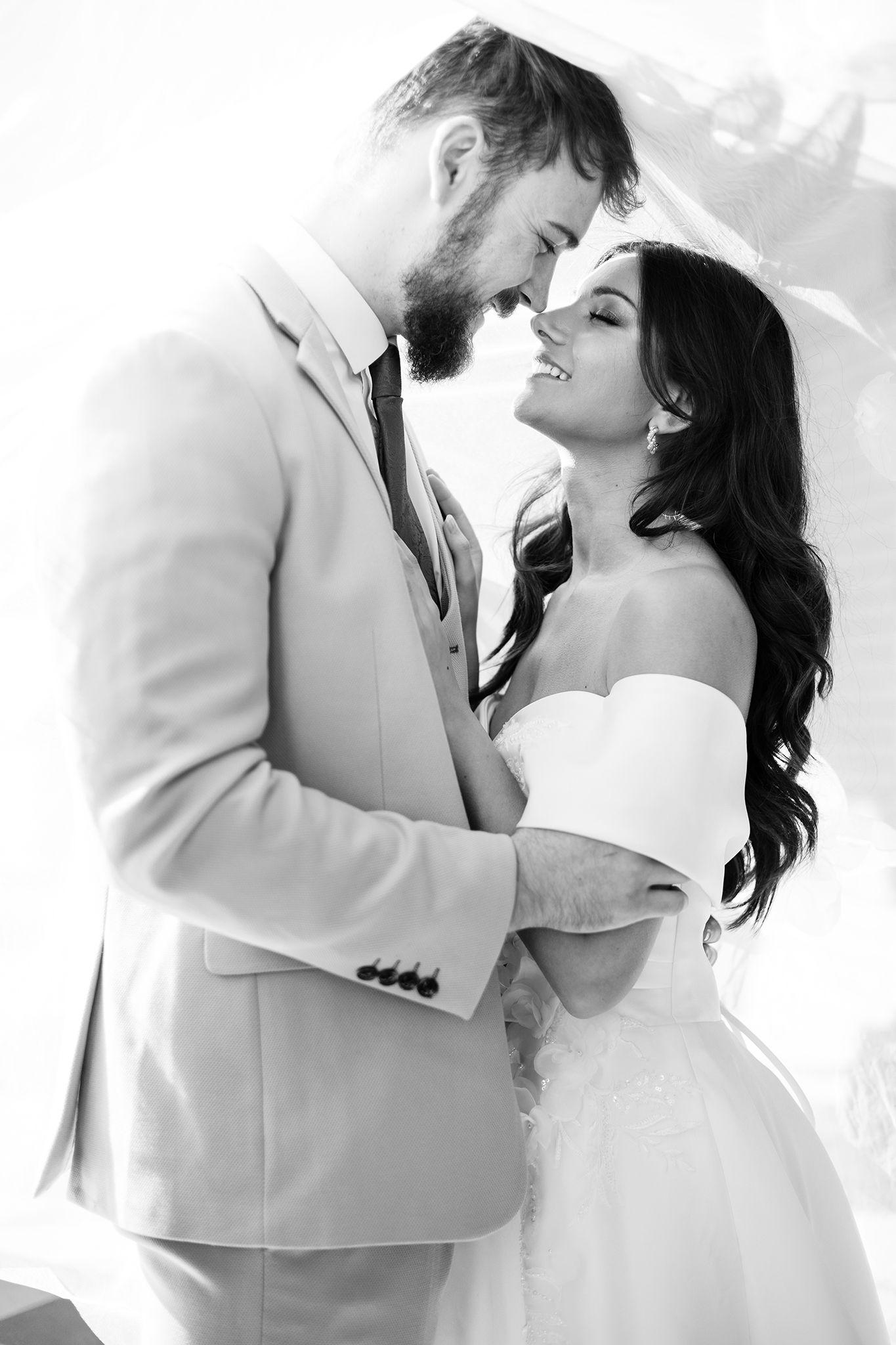 A romantic black and white wedding photo of a couple in elegant attire sharing an intimate moment together.
