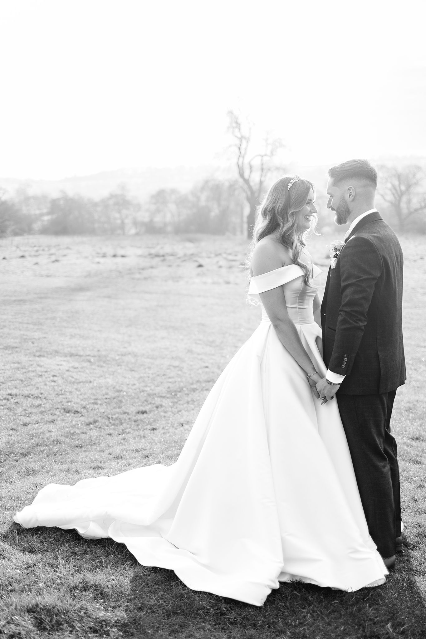 Black and white wedding photo of a couple sharing an intimate moment in an elegant off-shoulder gown and classic suit.