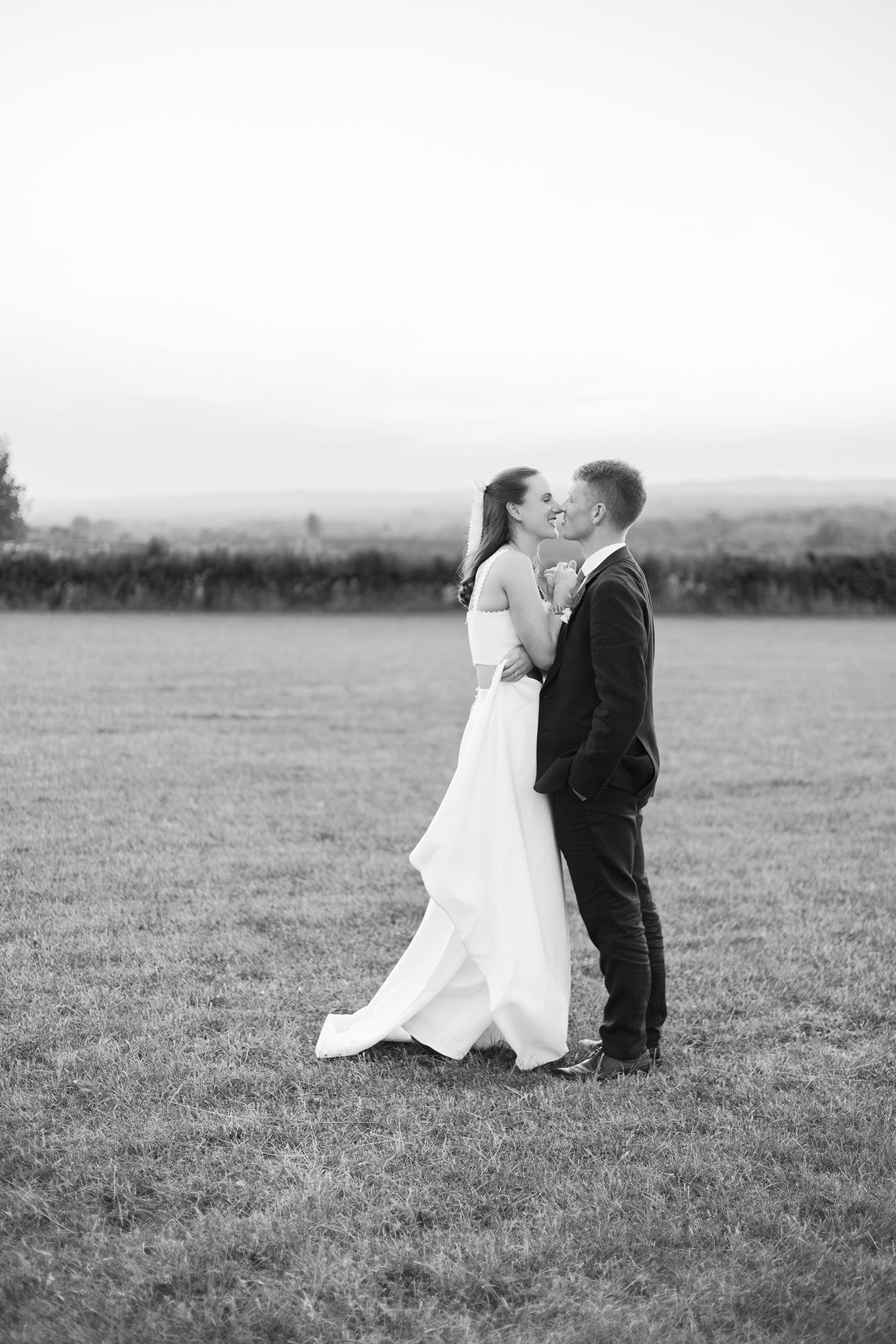 A romantic black and white wedding photo series showing a couple embracing in an open field with a misty landscape.