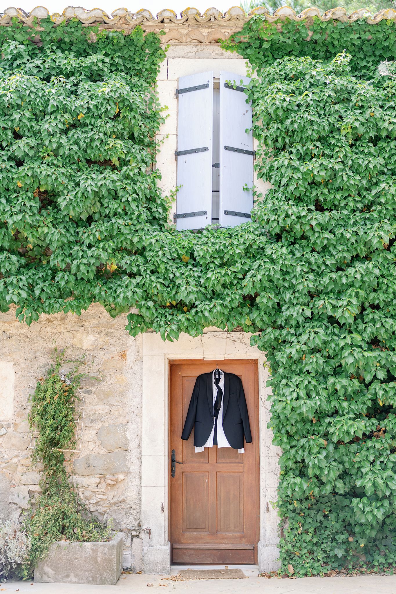 Black suit jacket hanging on a rustic wooden door of a stone building covered in lush green ivy.