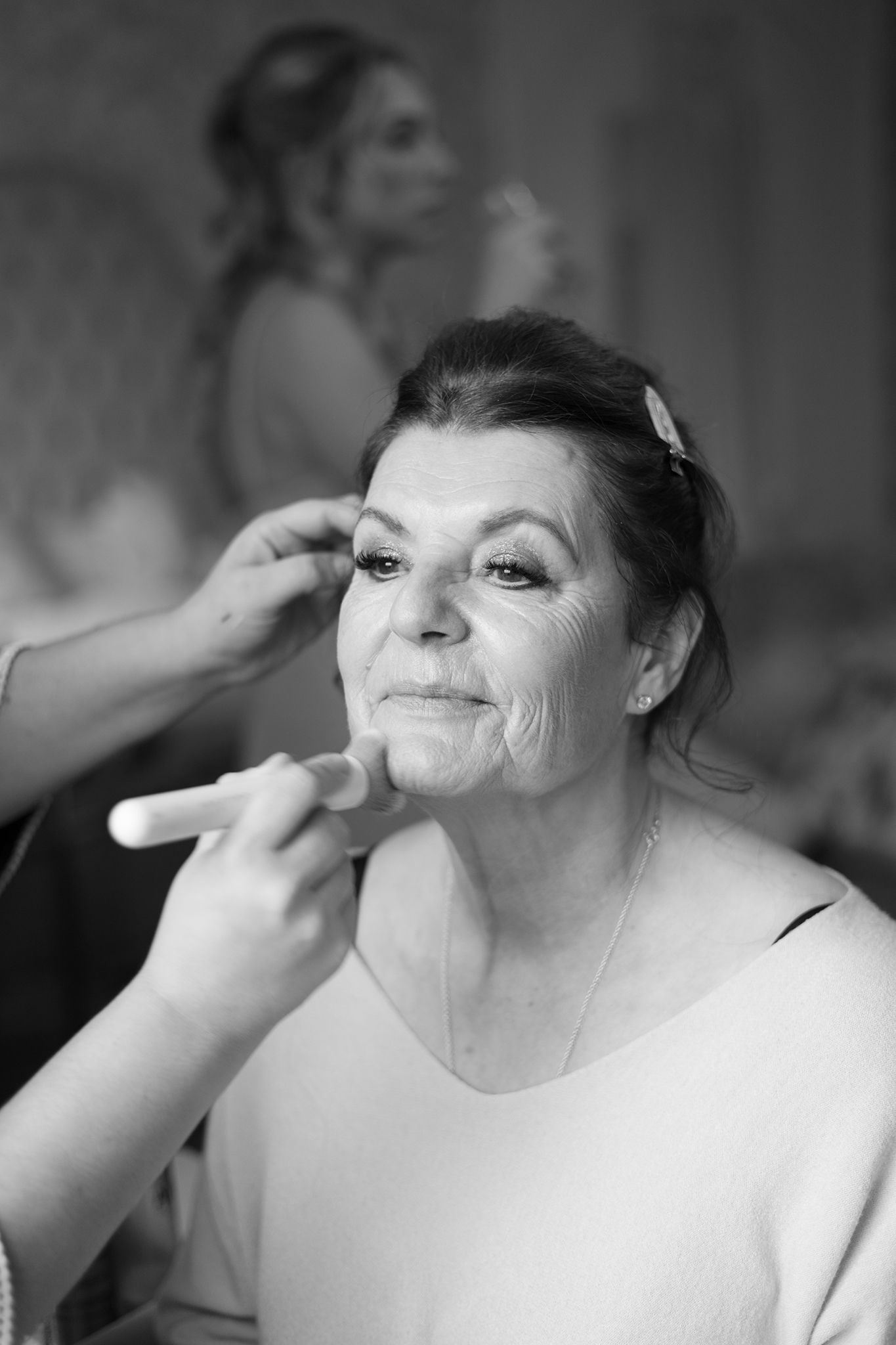 A sequence of black and white photos showing makeup being applied to a smiling woman's face during wedding preparations.