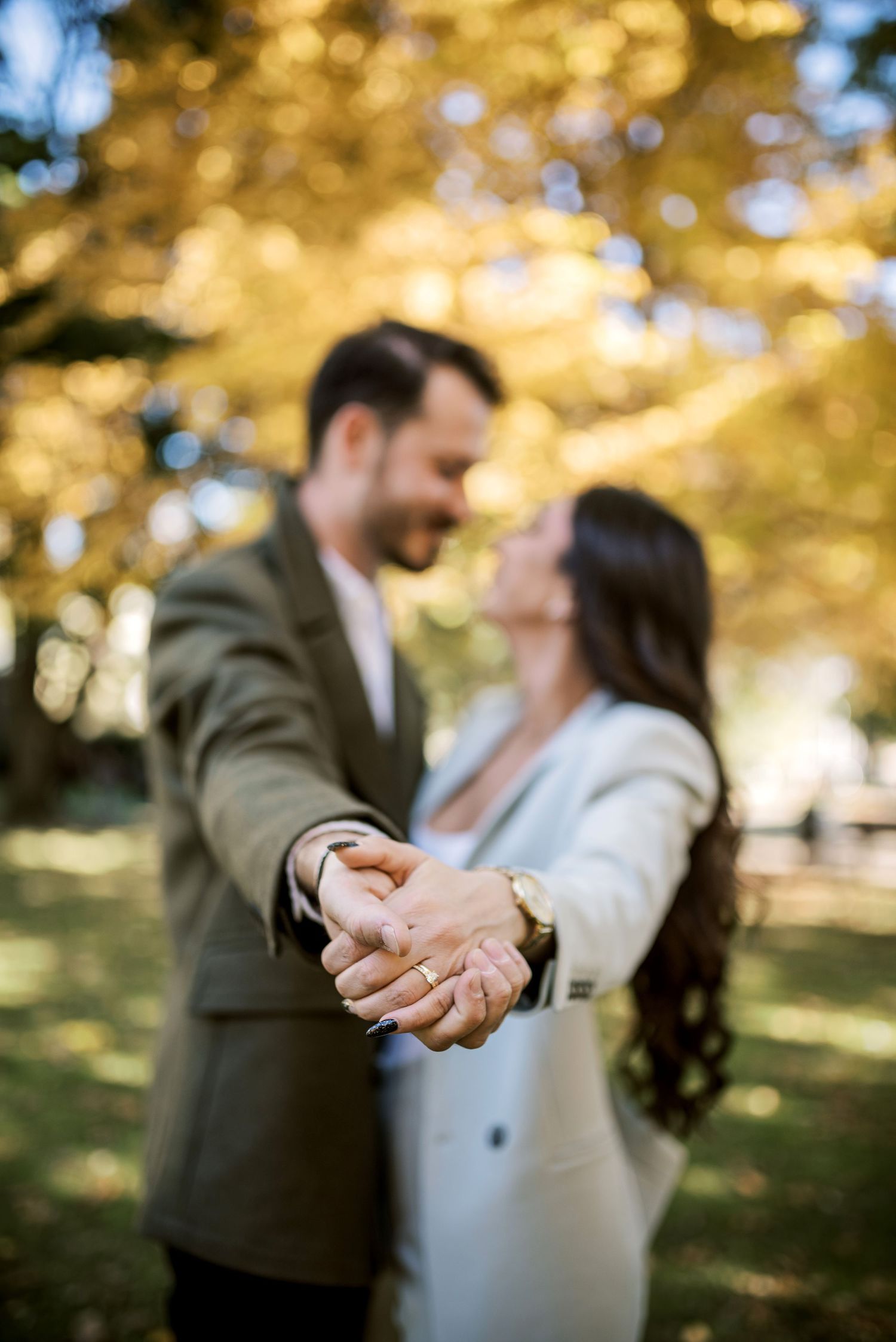 A romantic couple shares a tender moment in a park with golden autumn leaves in the background.