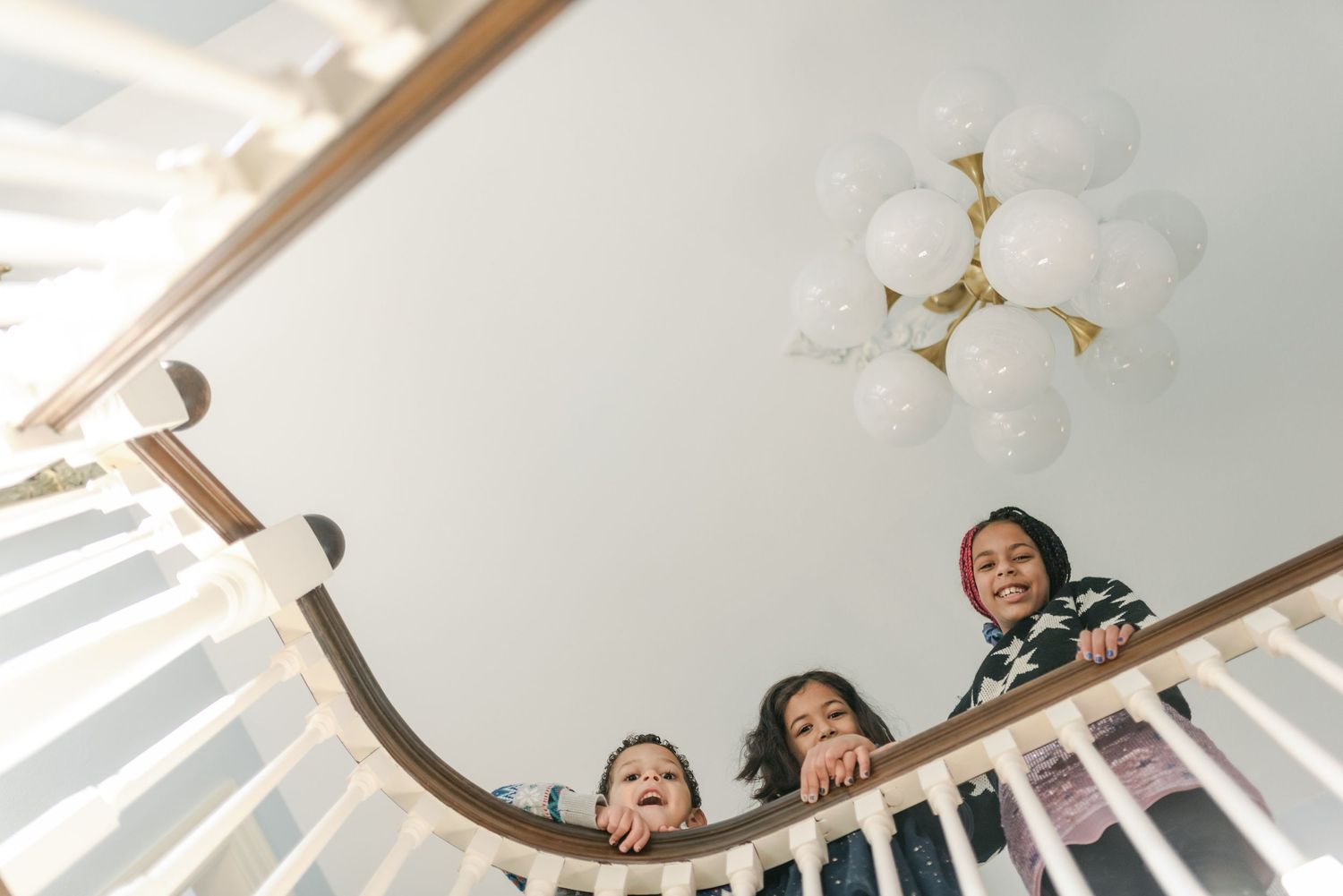 Looking down from below at three people peeking over a curved white railing with a decorative light fixture above.