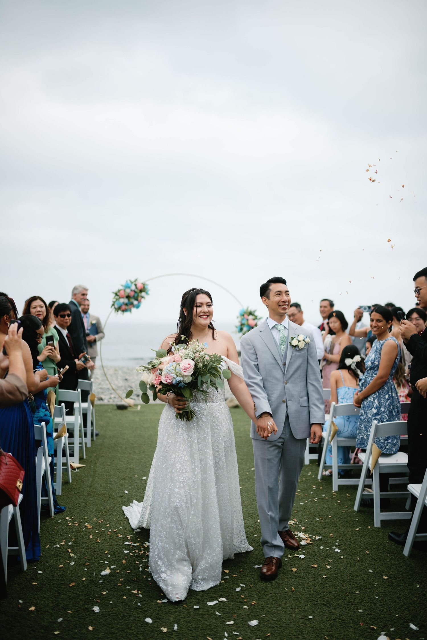 Celebration on a grassy hilltop with flower petals being tossed during an outdoor wedding ceremony.