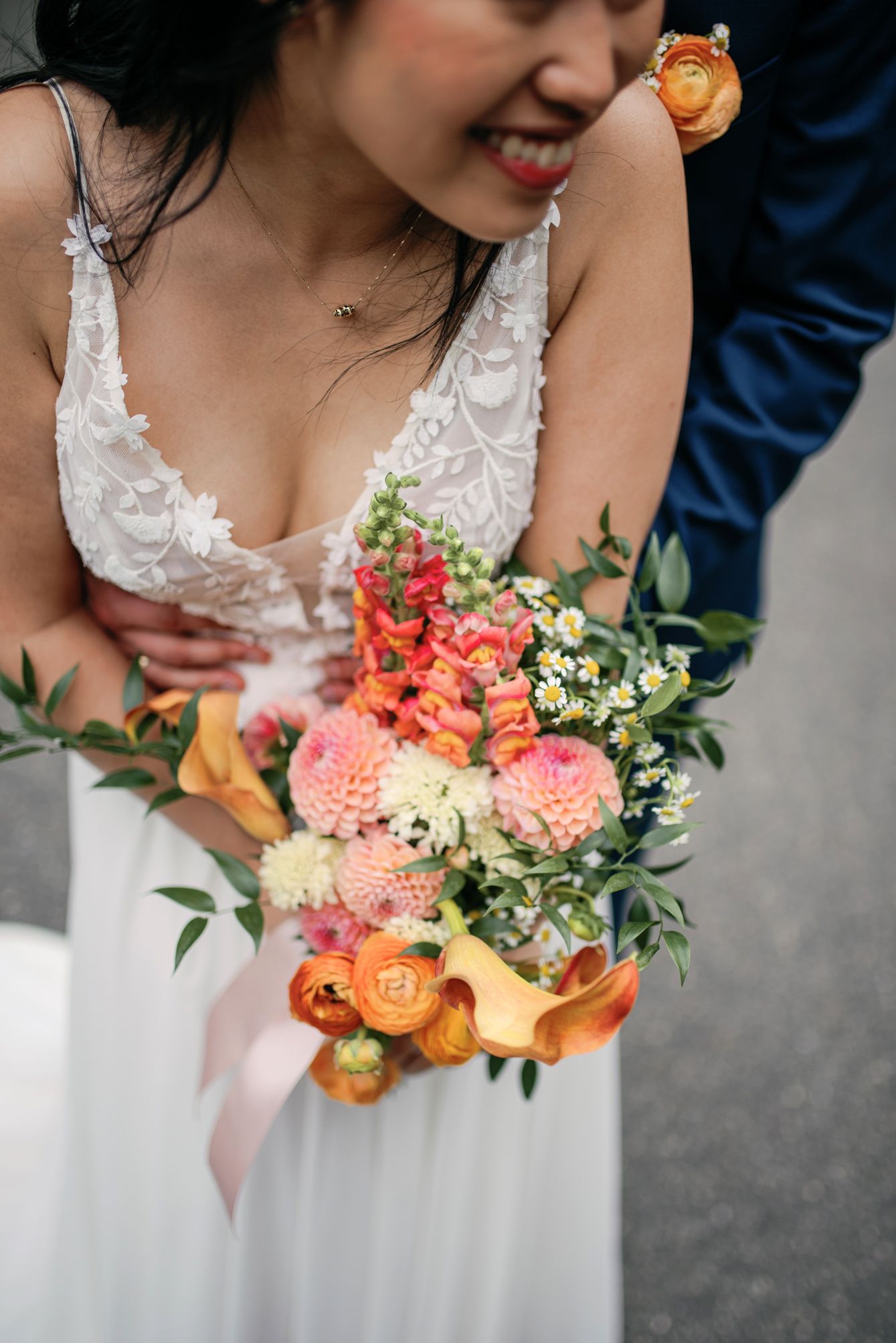 Close-up of a bride's lace dress and colorful wedding bouquet with coral and peach flowers.