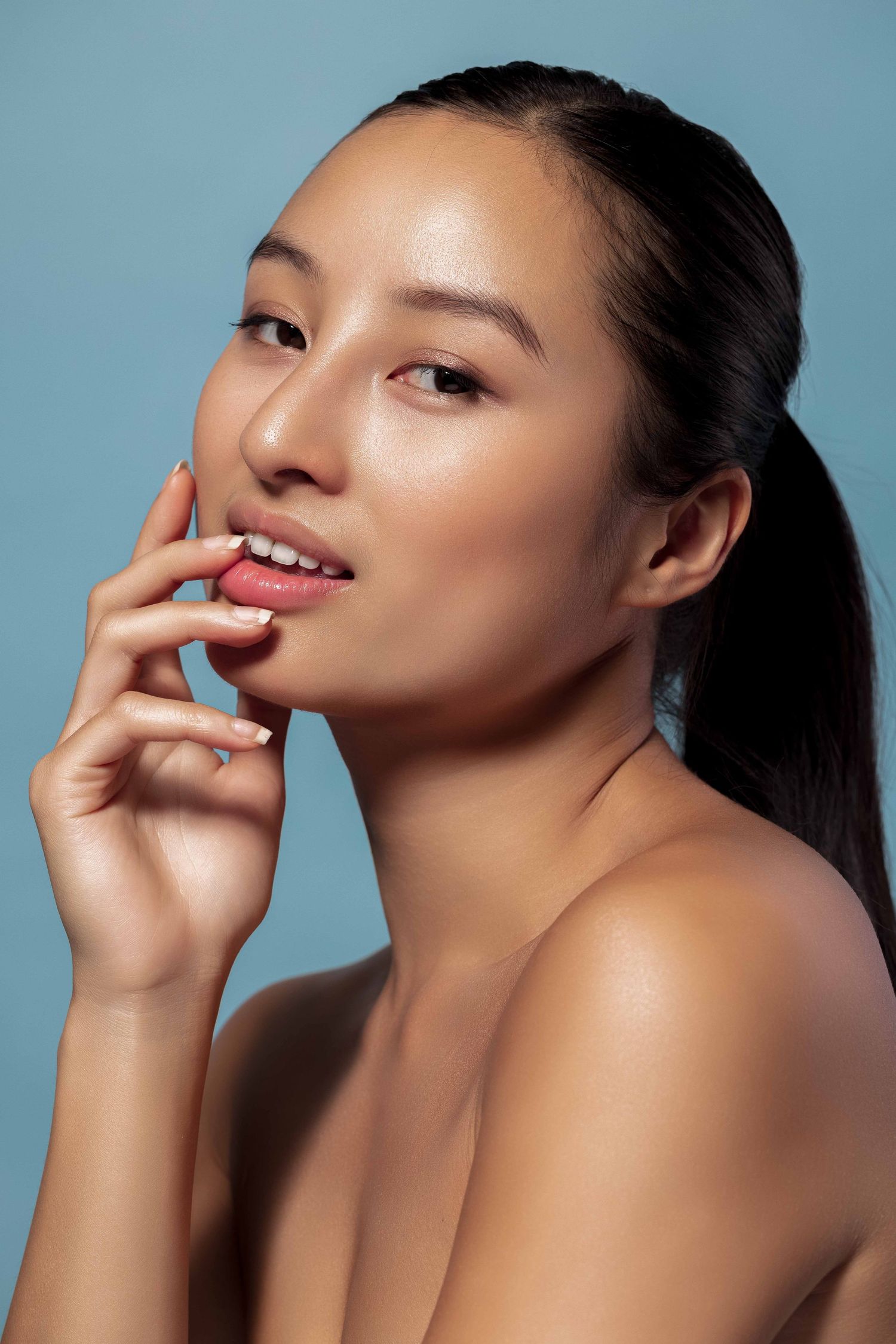 Portrait de beauté glamour avec une peau radieuse et un maquillage naturel sur fond bleu.